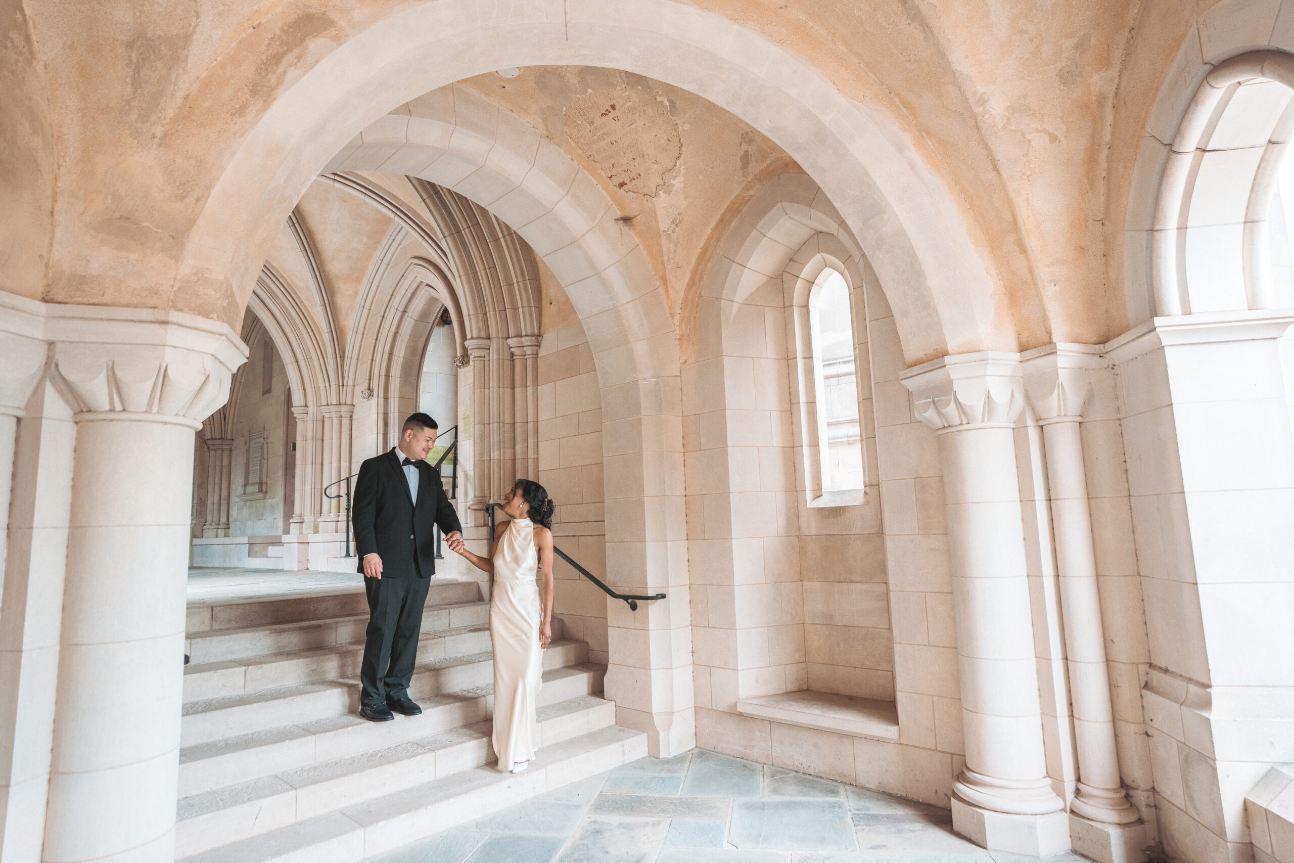 Couple walking hand in hand through stone archways inside a historic cathedral-inspired Washington DC location