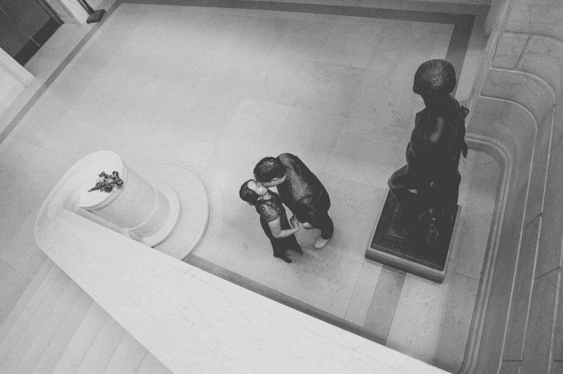 Black and white overhead portrait of couple kissing inside a museum atrium with dramatic architectural lines