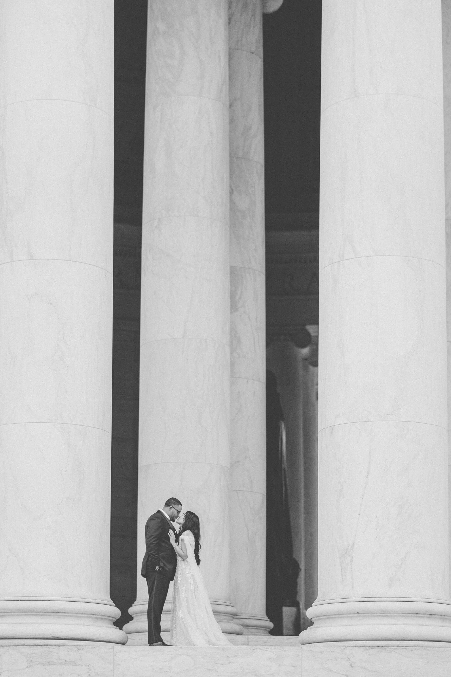Black and white portrait of couple standing between towering marble columns during an elegant Washington DC engagement session