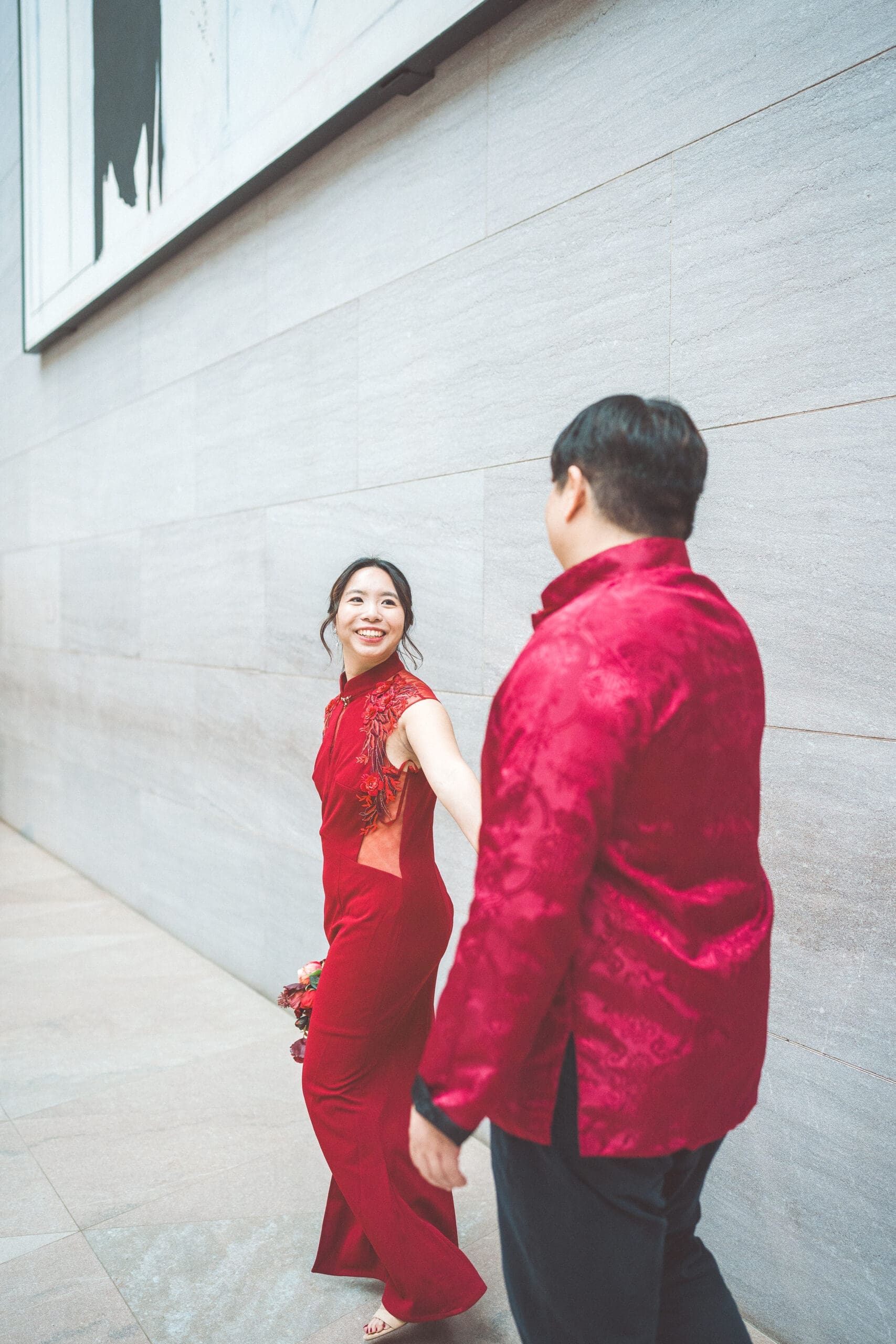 Couple in traditional red attire walking hand in hand through the city during a cultural engagement portrait session