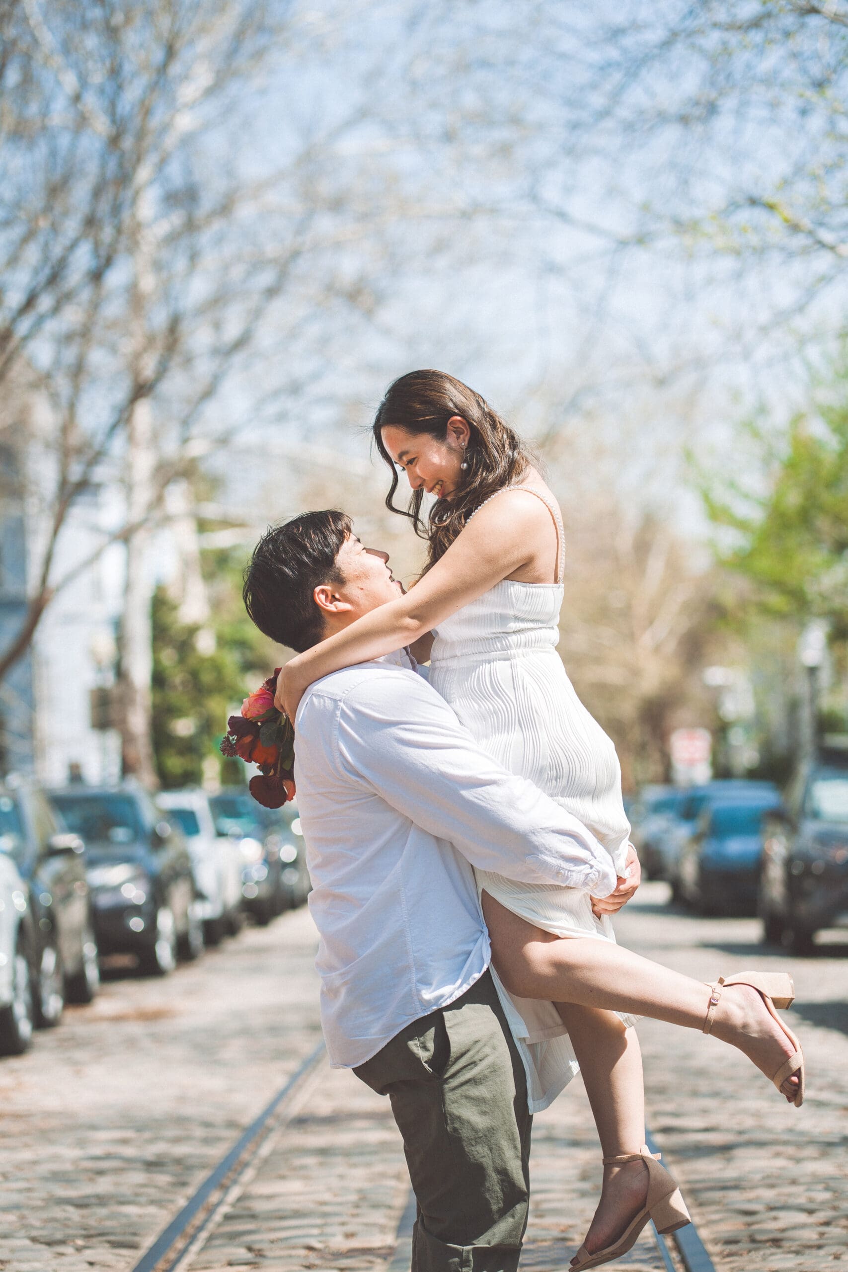 Joyful engagement photo of groom lifting partner in the middle of a charming tree-lined city street