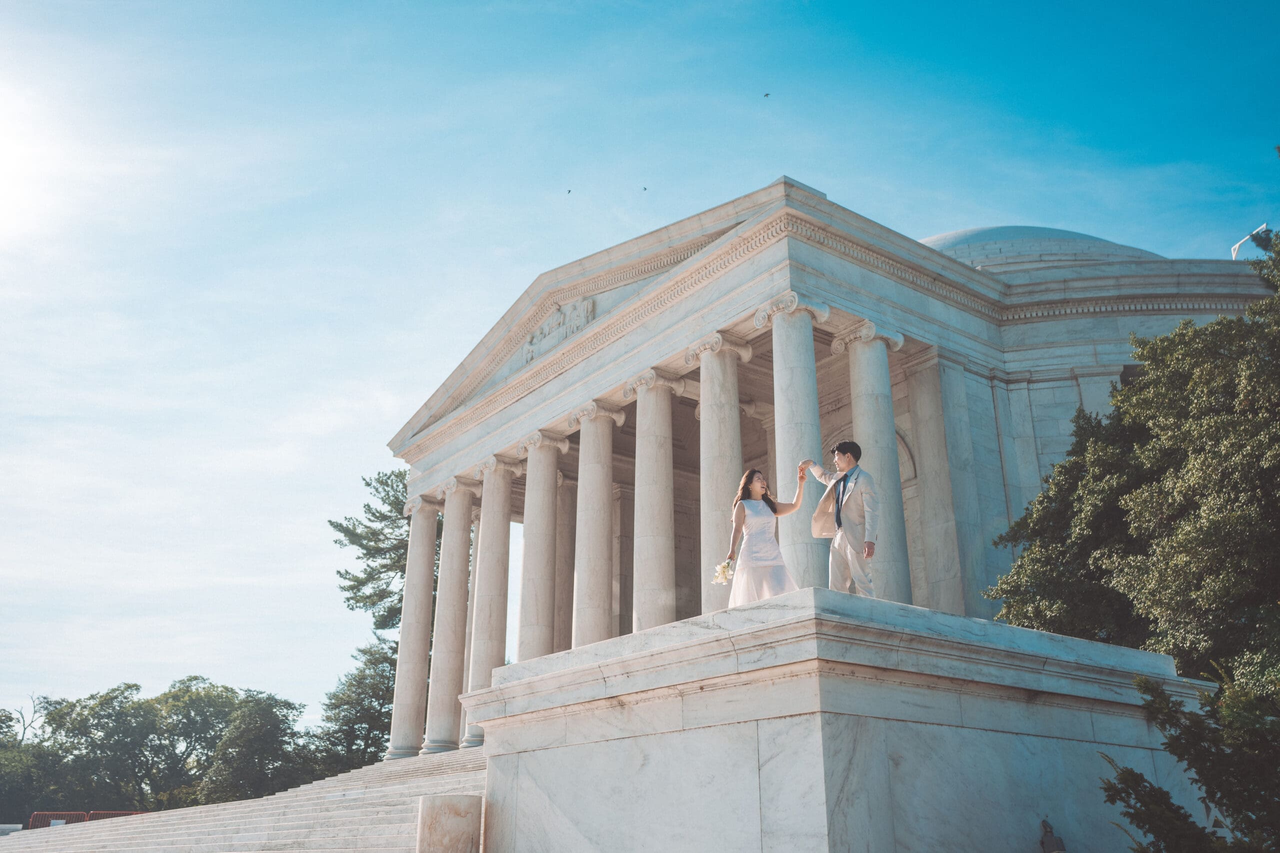 Wide architectural portrait of couple celebrating their engagement at the Jefferson Memorial during golden morning light