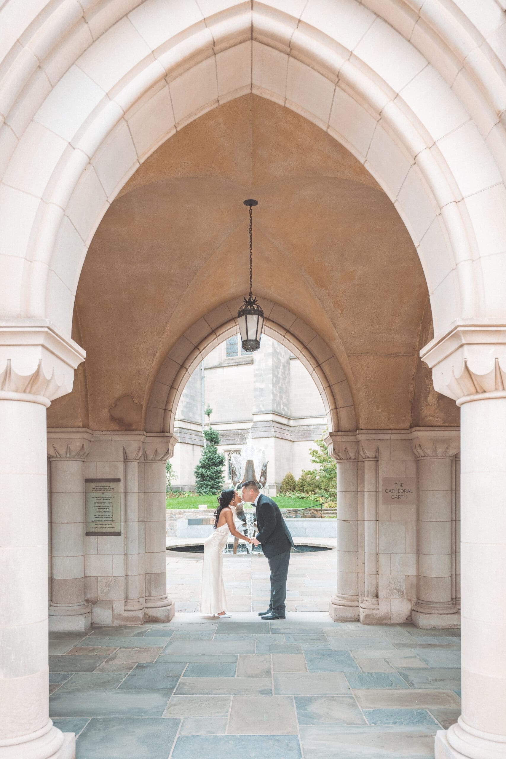 Couple leaning in for a kiss beneath a grand stone archway in a timeless Washington DC engagement portrait