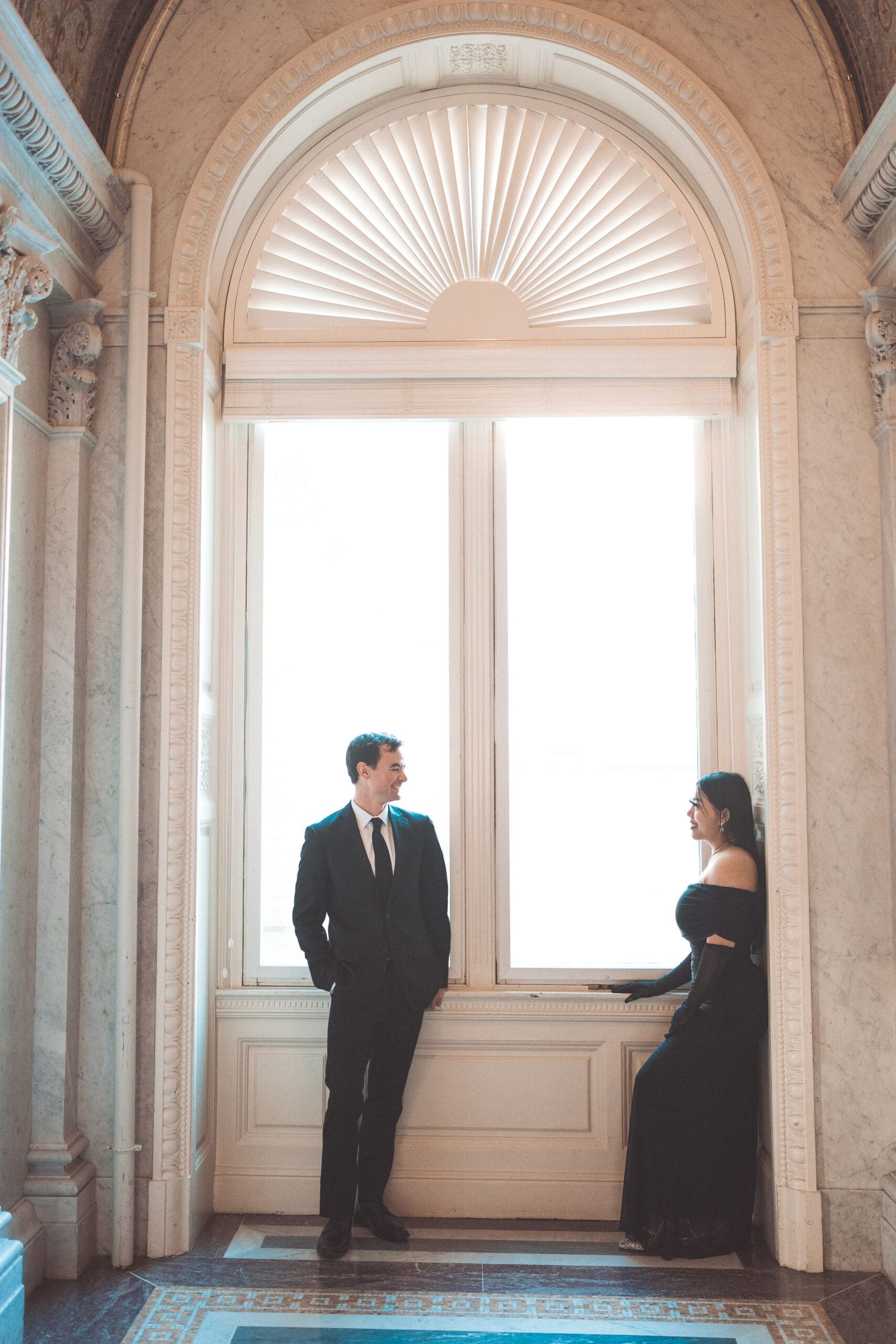 Fashion-forward couple posing in front of tall sunlit windows inside a historic Washington DC landmark