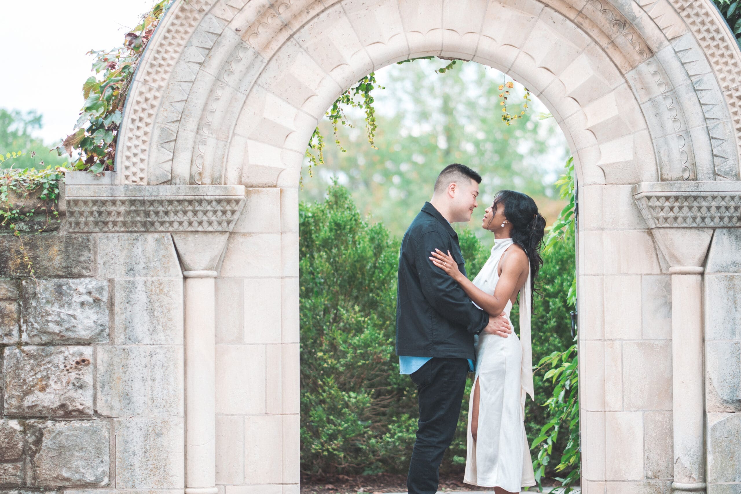 Romantic portrait of couple embracing beneath a stone garden arch surrounded by lush greenery during a Washington DC engagement session