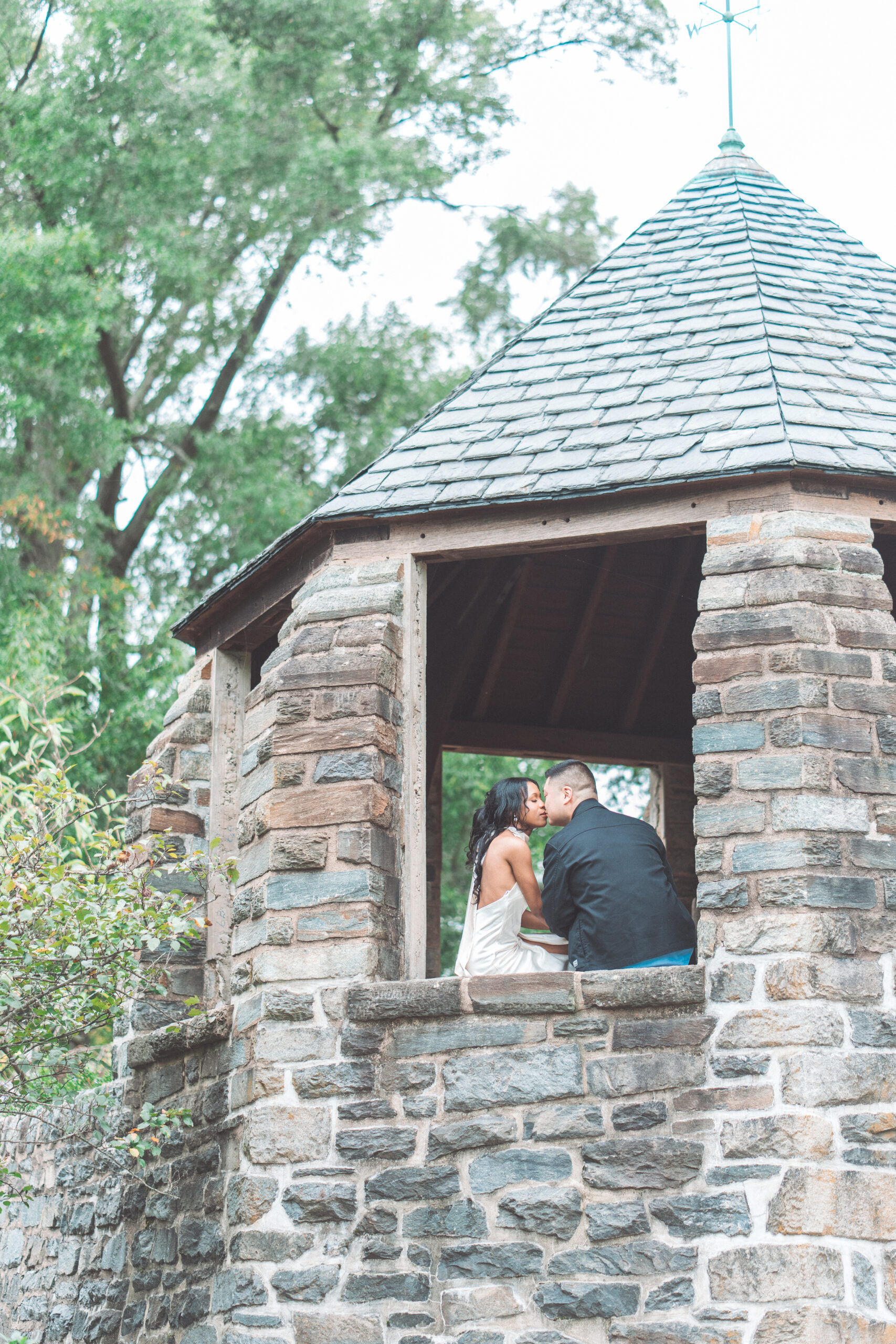 Intimate portrait of couple kissing inside a charming stone gazebo surrounded by greenery