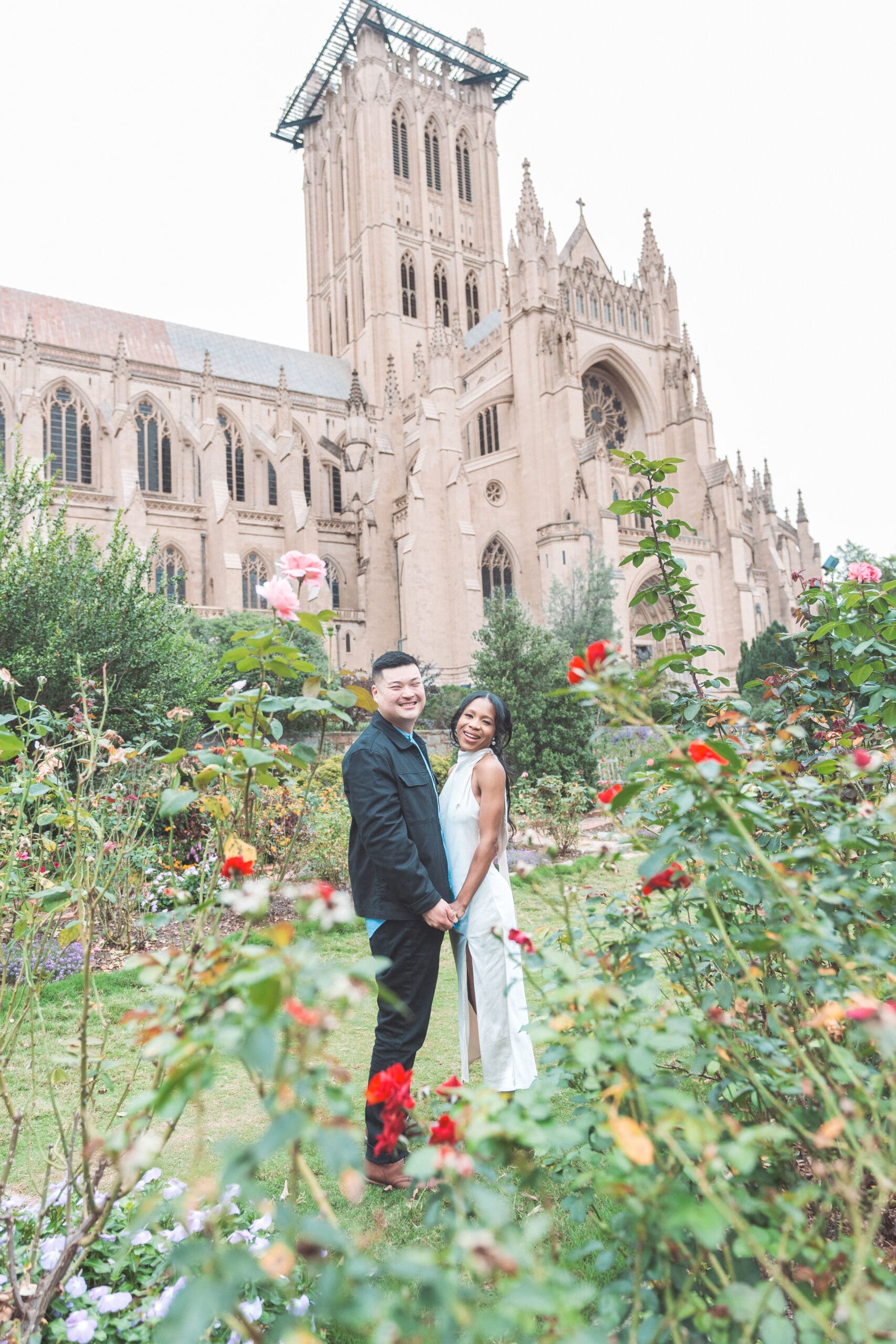 Couple standing in a rose garden with the Washington National Cathedral in the background during their Washington DC engagement