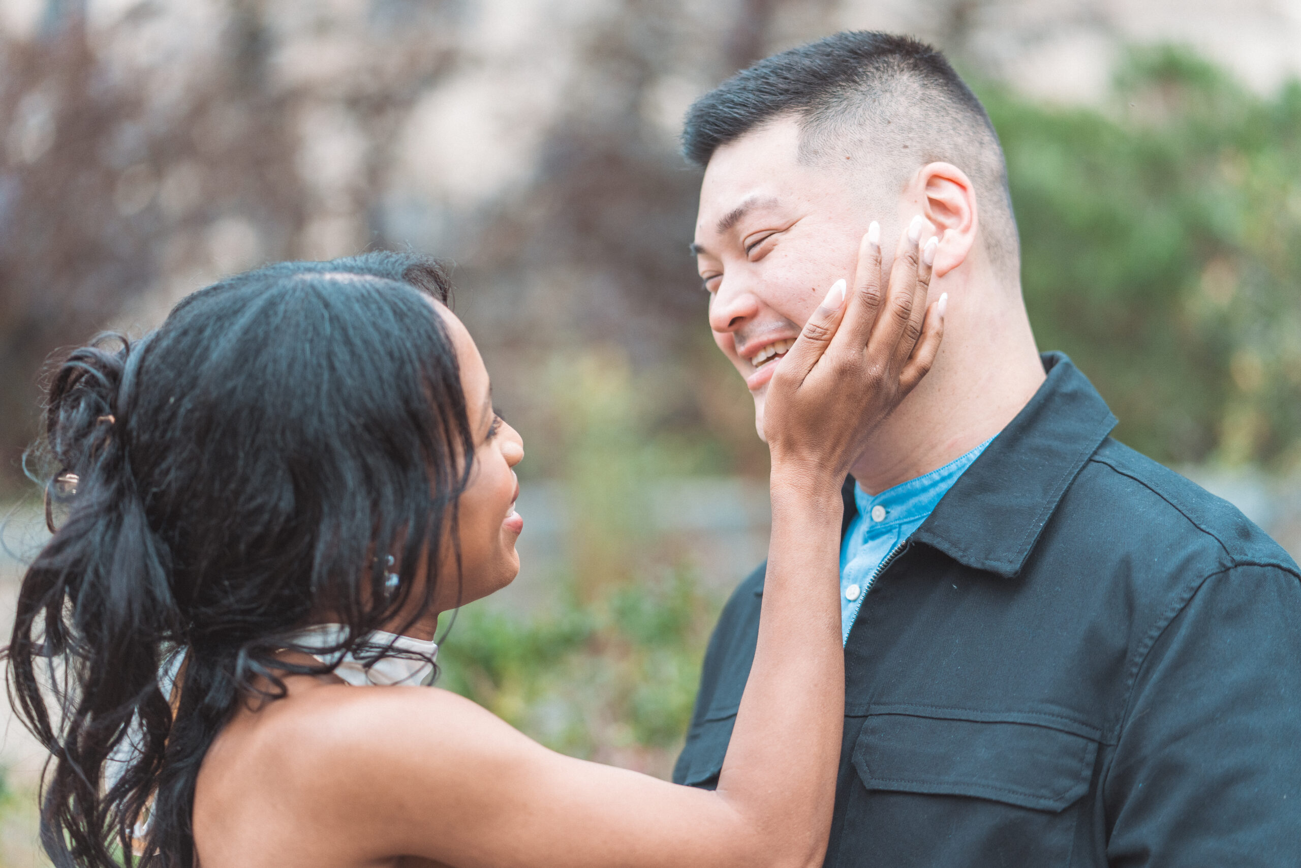 Close-up candid engagement portrait of couple smiling at each other in a quiet garden setting
