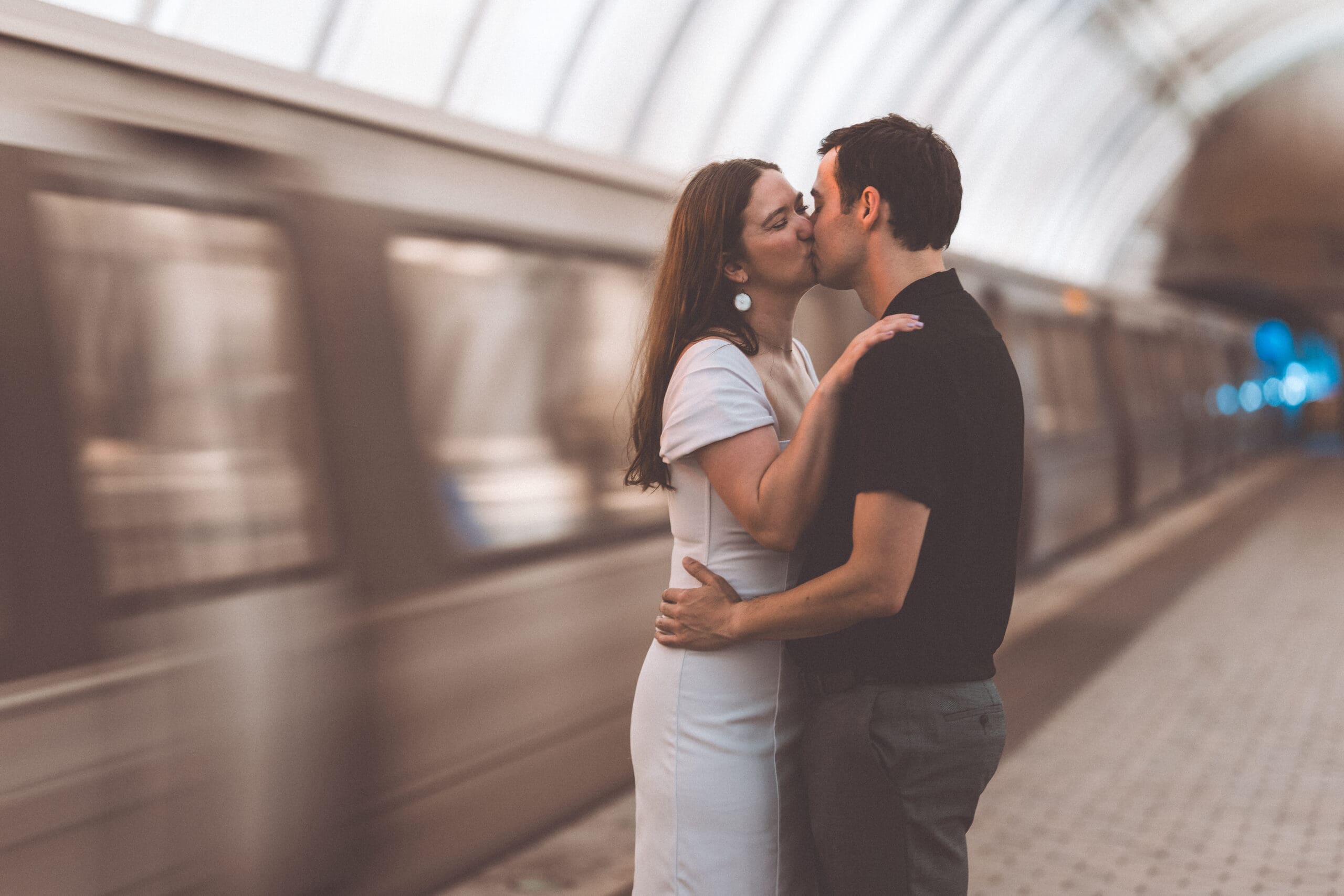Soft romantic portrait of a couple kissing on the metro platform with a blurred train in the background