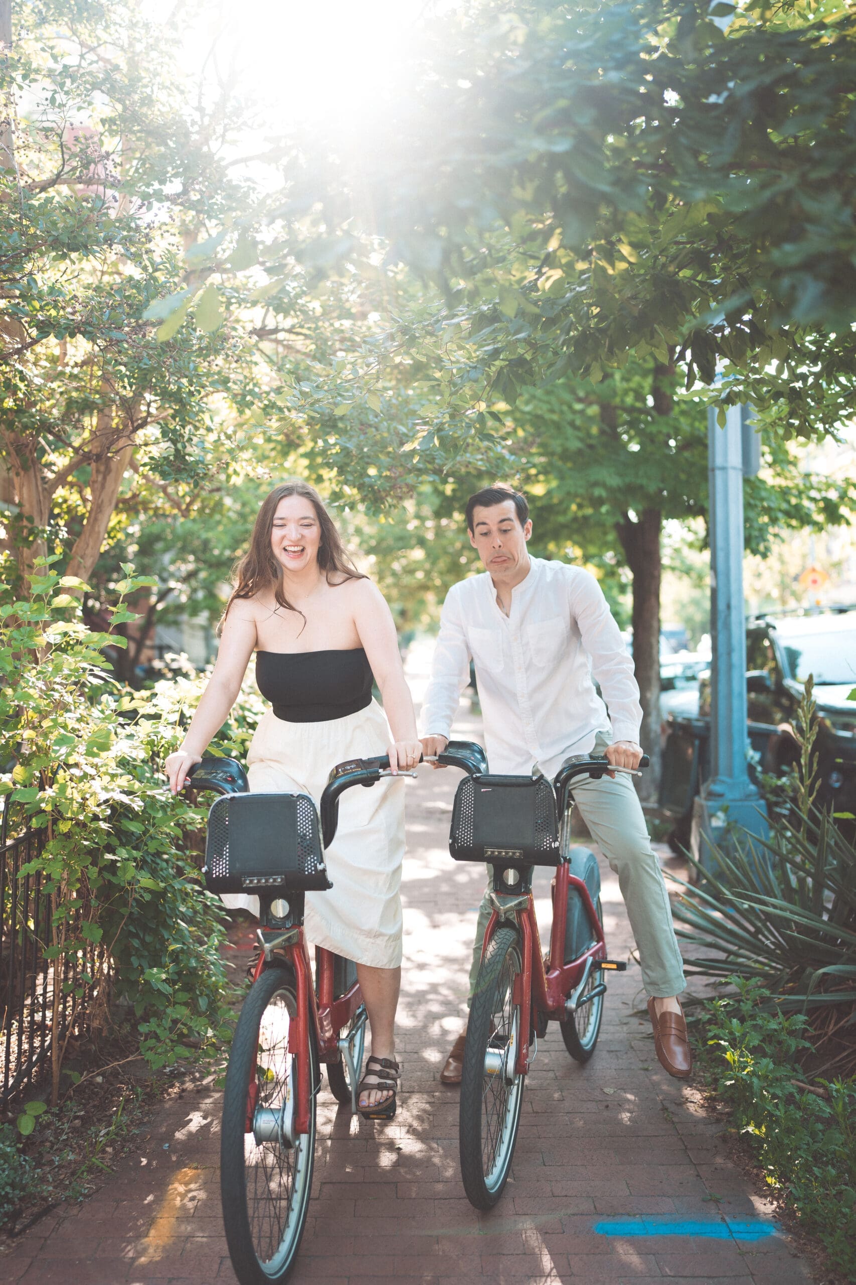 Fun candid of a couple riding Capital Bikeshare bikes together on a sunny DC sidewalk during Washington DC engagement photos