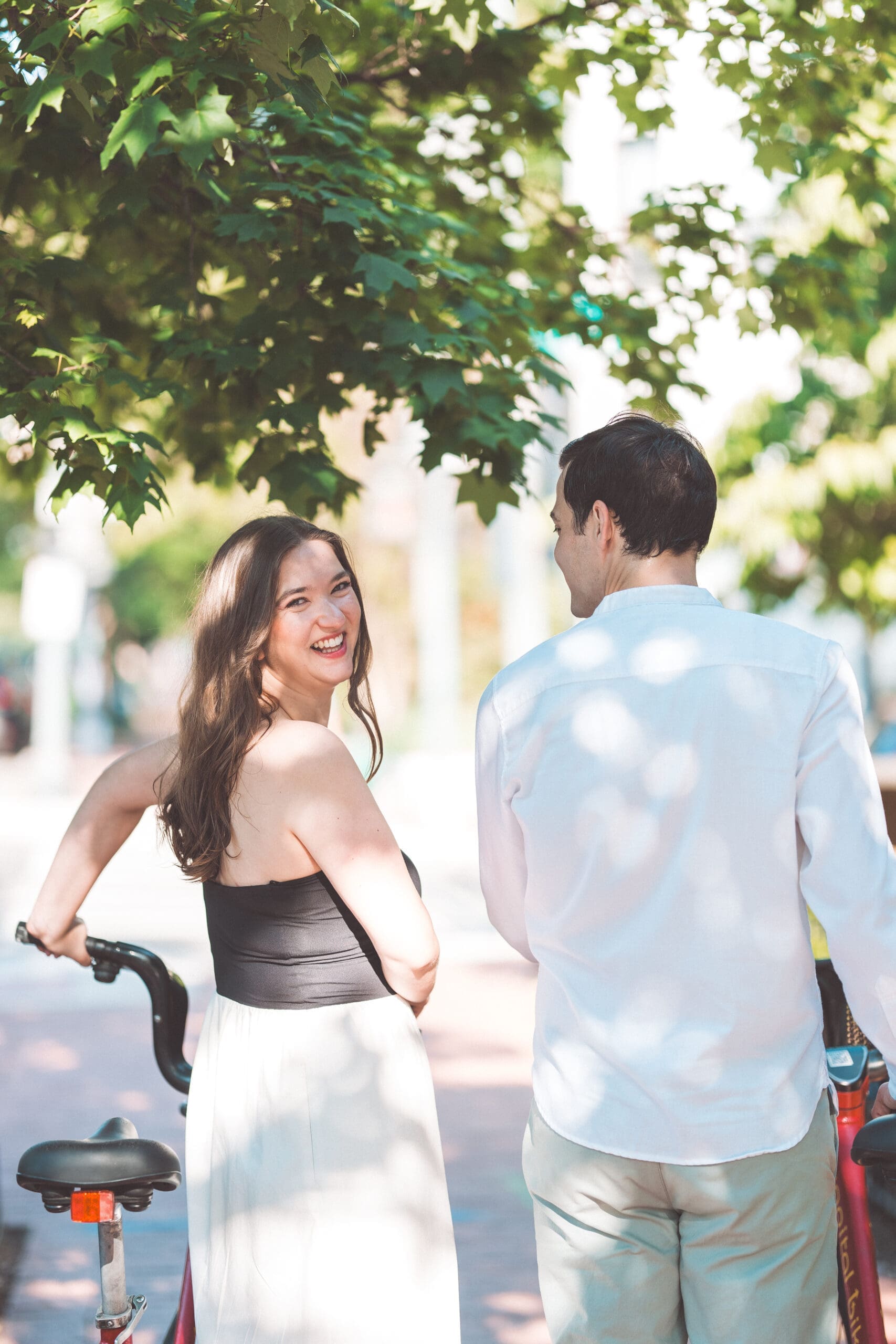 Joyful candid of a couple walking beneath leafy trees in Georgetown during their Washington DC engagement photos