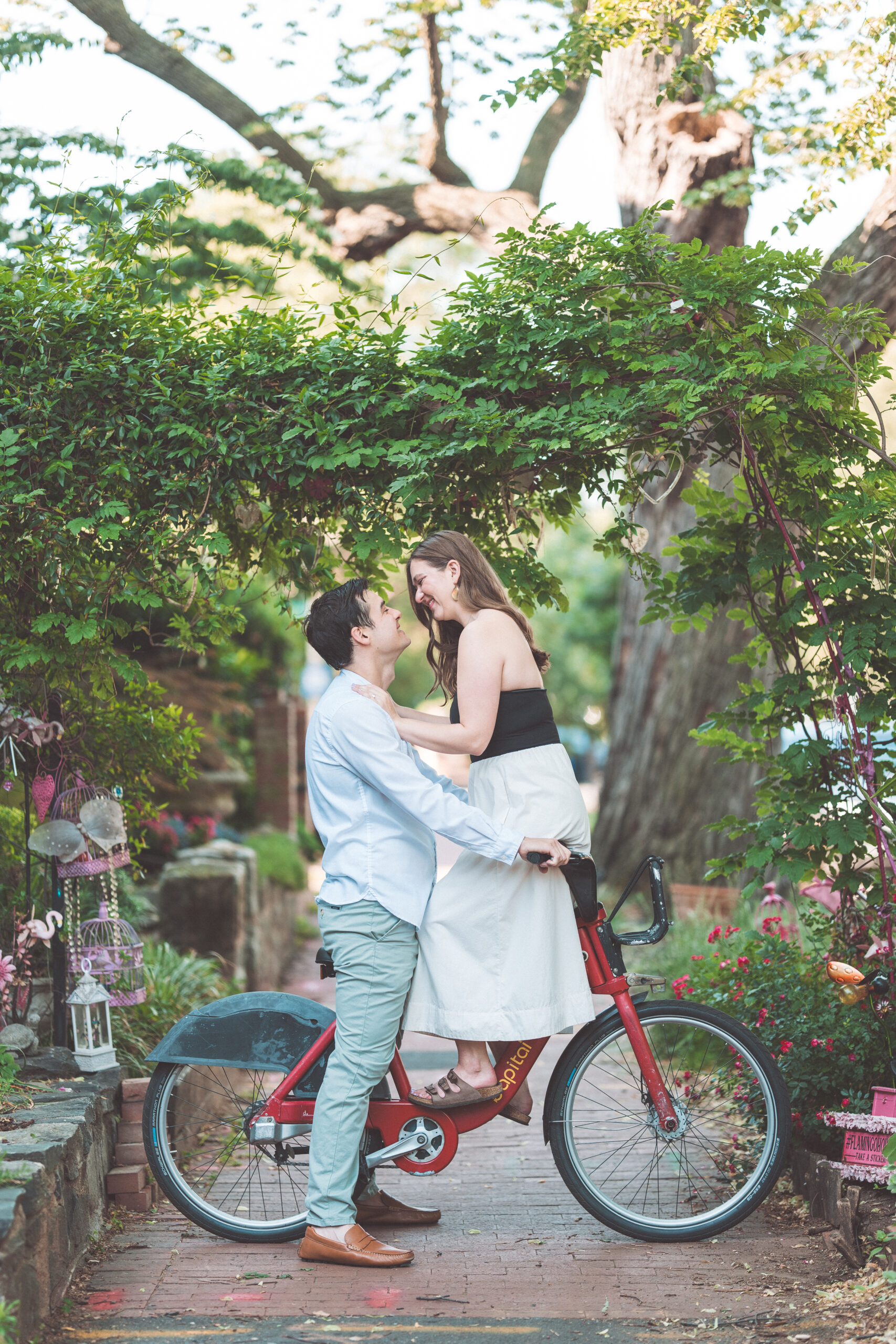 Romantic portrait of an engaged couple embracing beneath a lush garden arch with a Capital Bikeshare bike