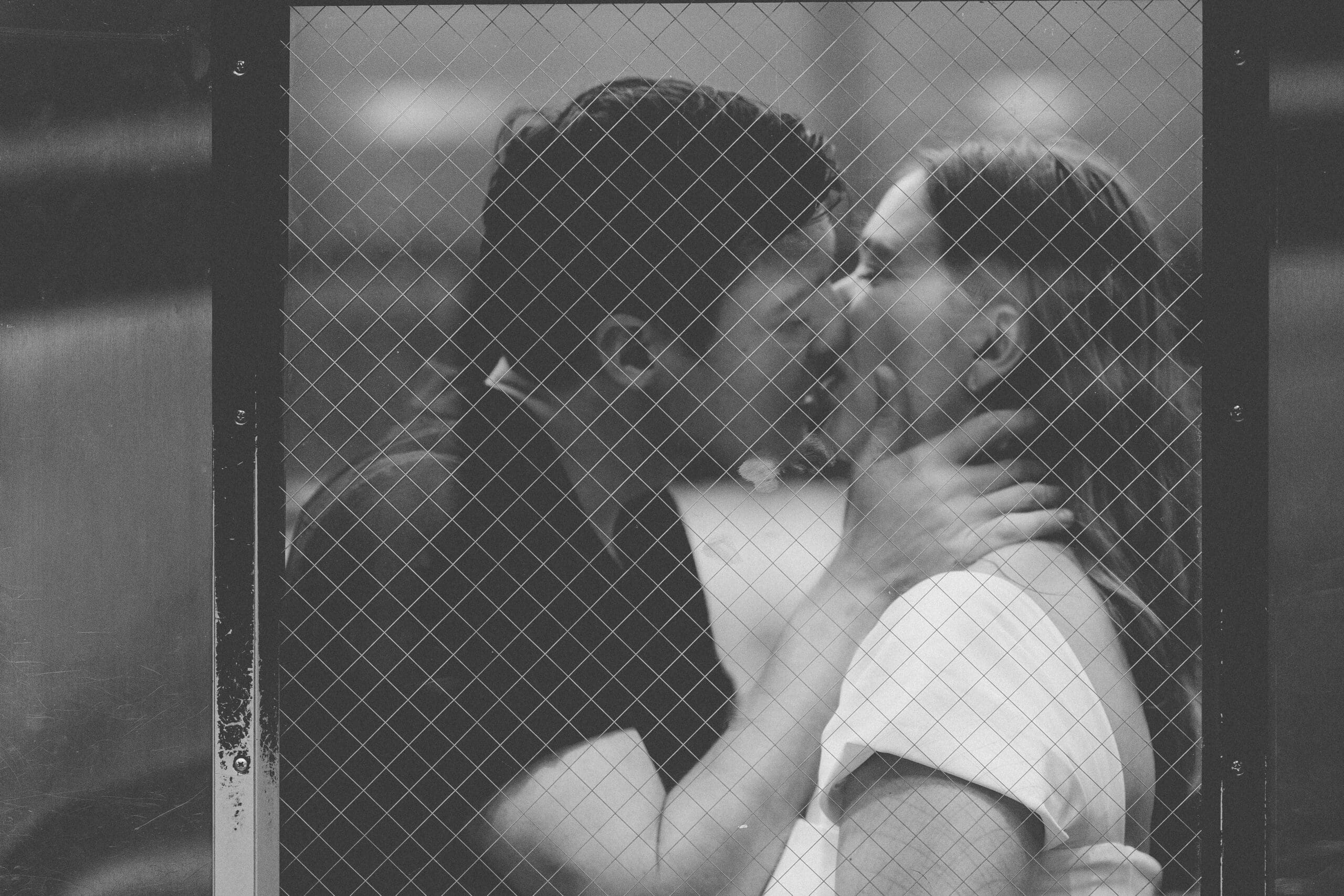 A romantic black and white image of a couple sharing a kiss through the window of a subway car.