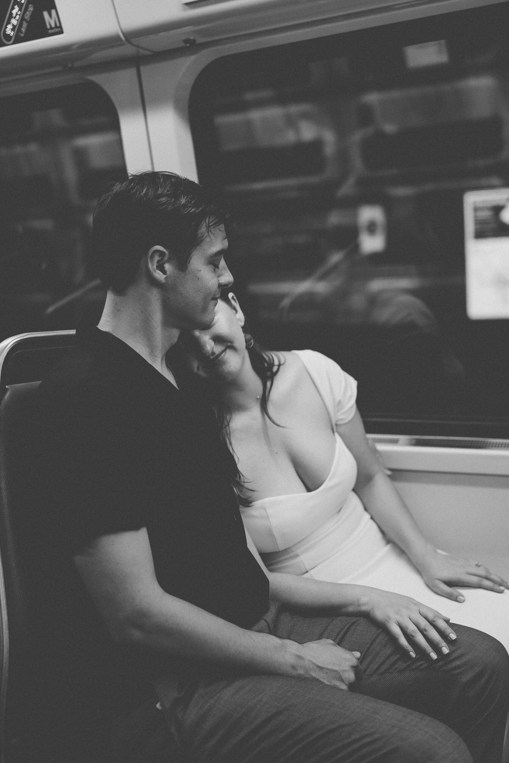 Black and white candid of an engaged couple sitting together on the metro, sharing a quiet intimate moment
