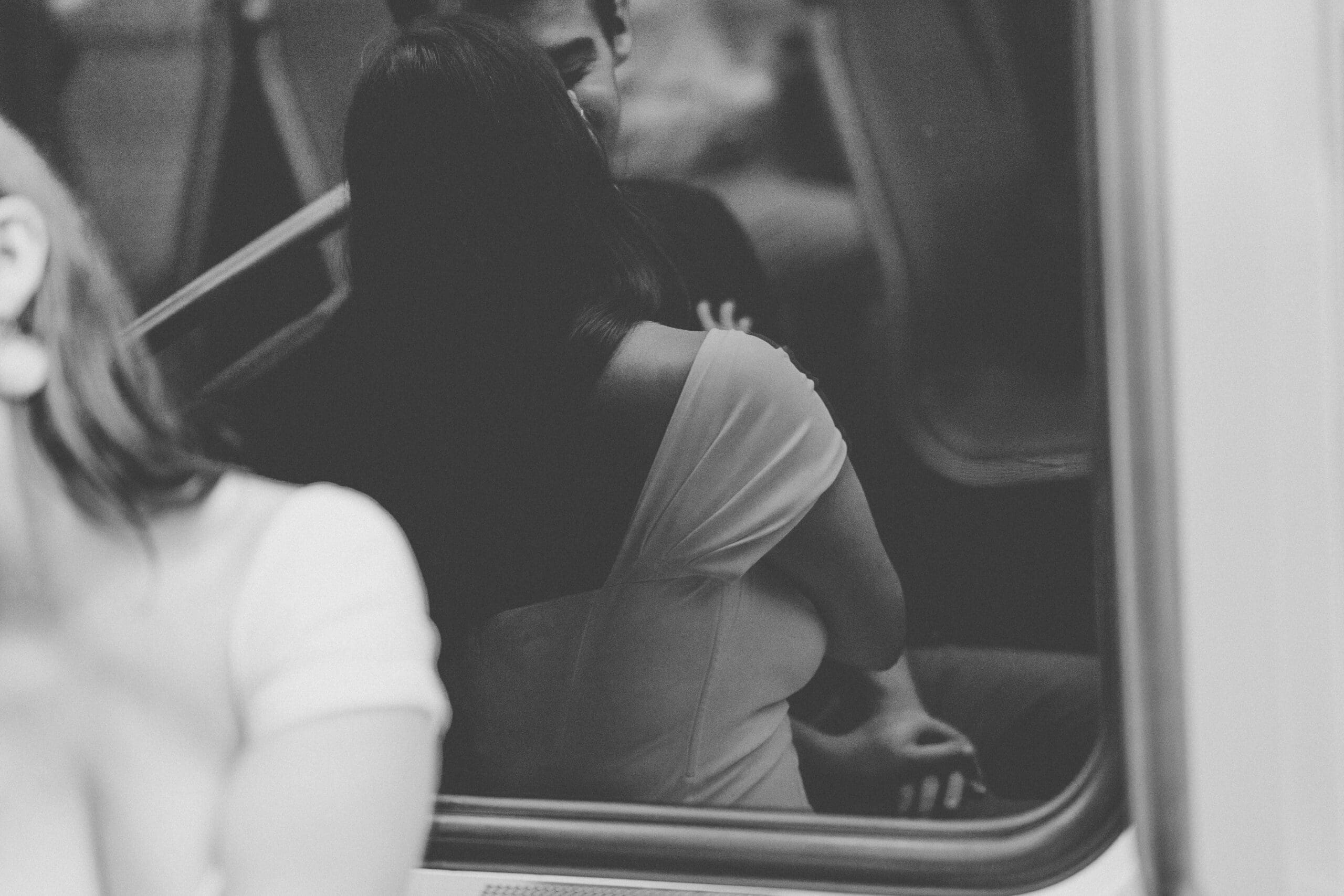 Black and white candid reflection of a couple embracing inside a Washington Metro train