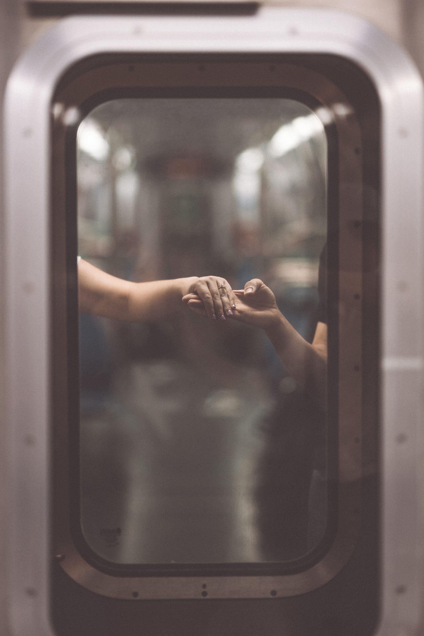 A portrait of a couple holding hands in the window of a subway car.