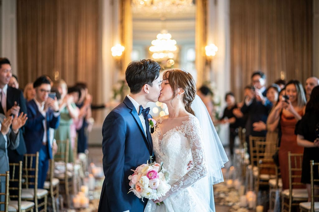 Newlyweds sharing their first kiss as guests celebrate during their ceremony at The Belvedere Maryland.