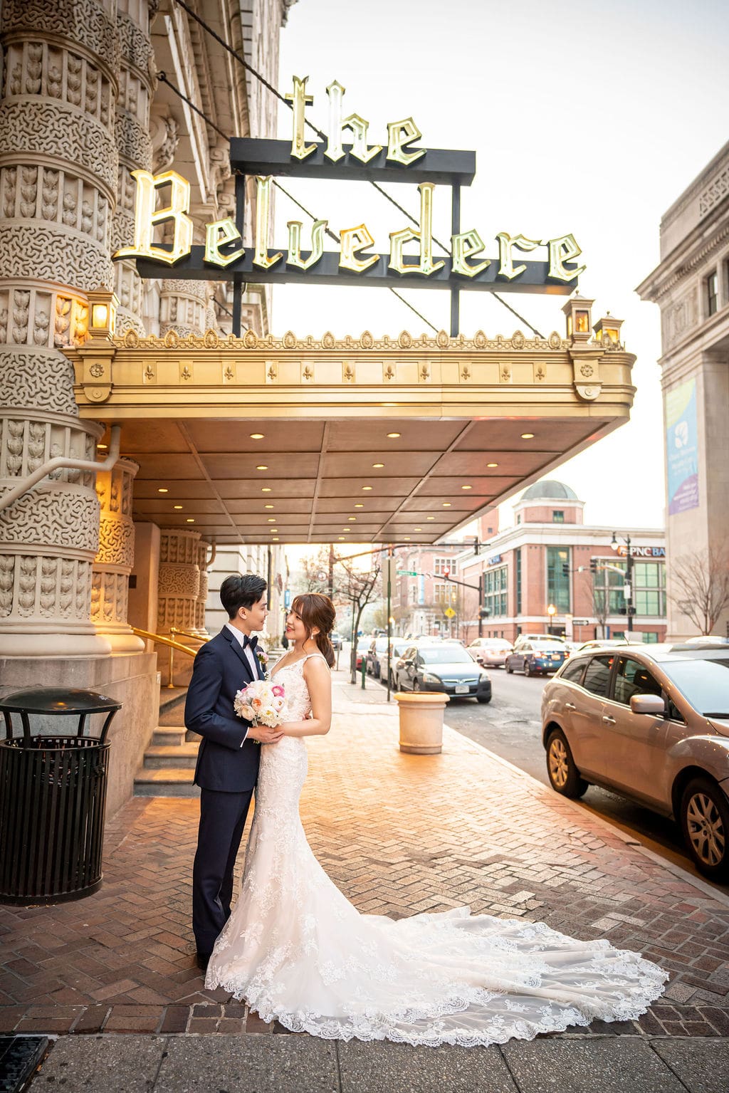 Korean bride and groom posing beneath the marquee entrance of The Belvedere Maryland in downtown Baltimore on their wedding day.