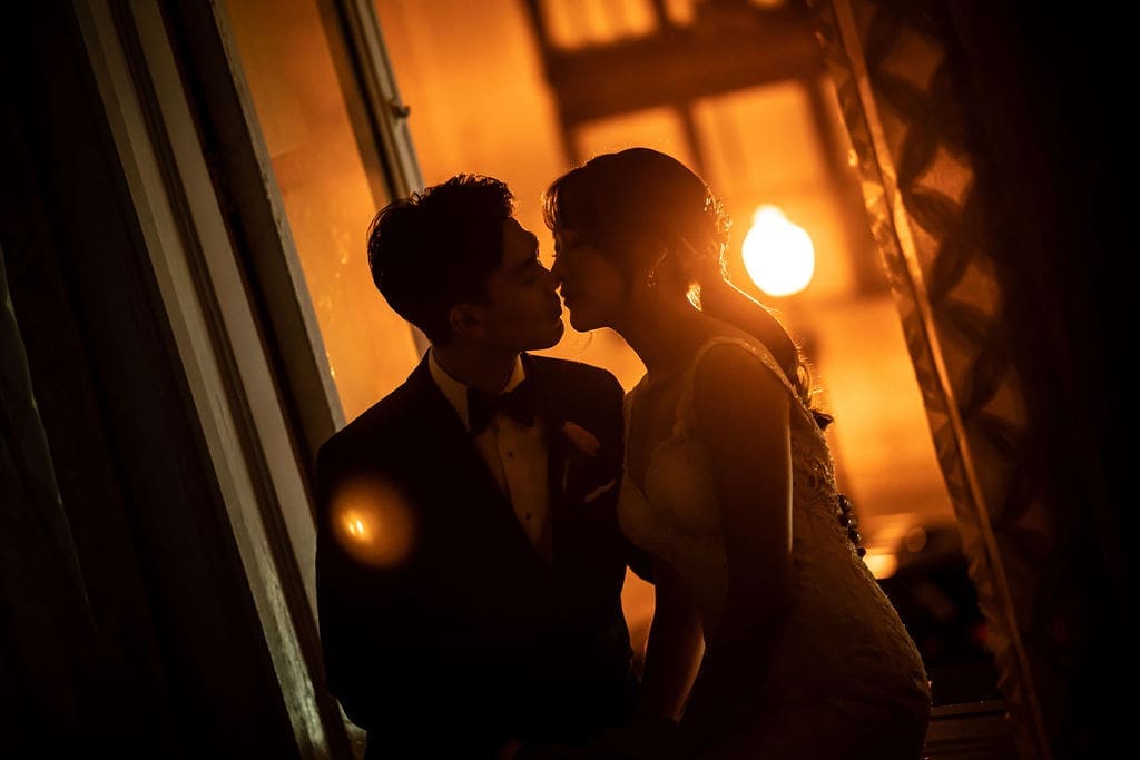 A moody and intimate portrait of a bride and groom sharing a kiss in dim light.
