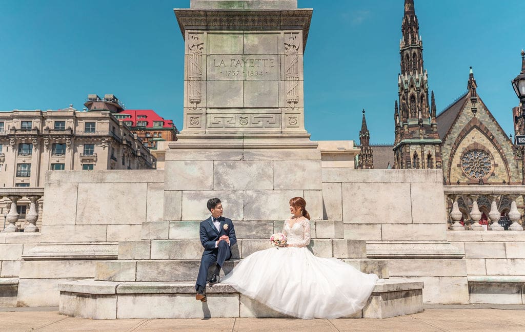 Korean bride and groom seated together at the Lafayette Monument in Baltimore for wedding portraits.