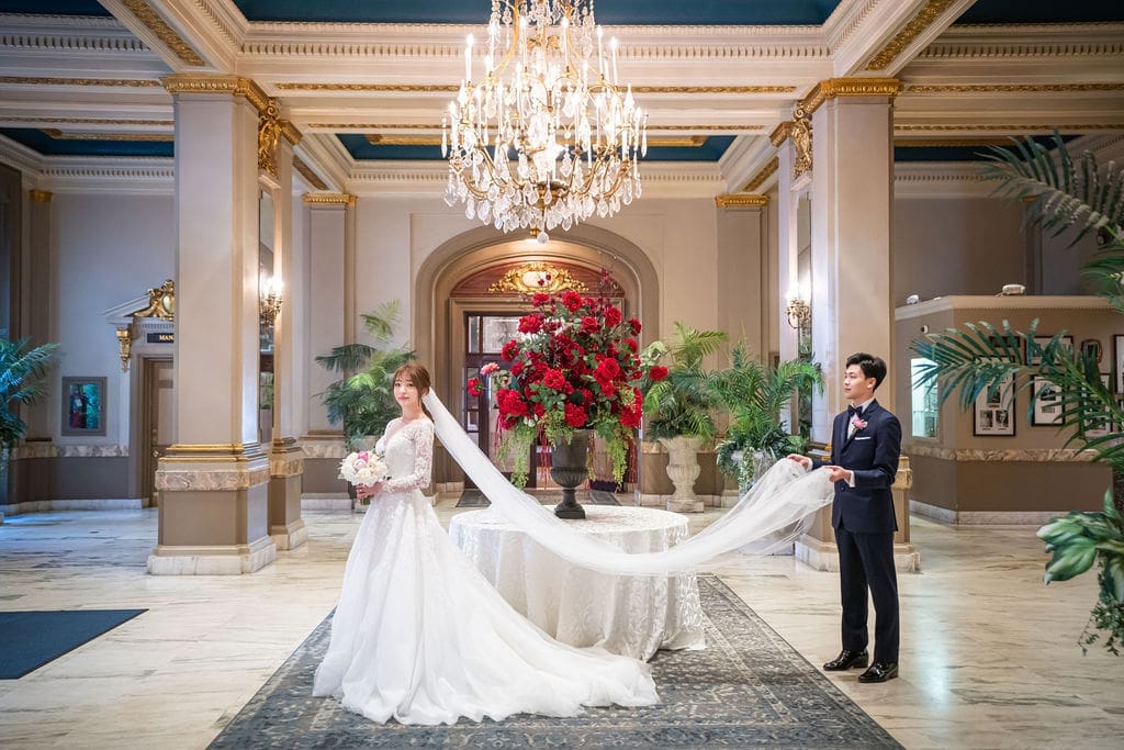 Korean bride and groom posing with a flowing cathedral veil in the grand lobby of The Belvedere Maryland.