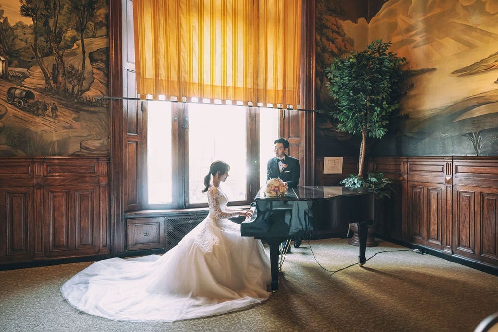 Bride playing piano while the groom watches in an elegant wood-paneled room at The Belvedere Maryland.