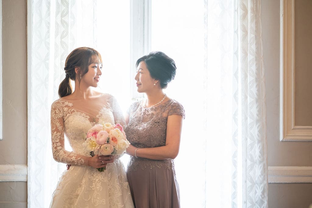 Mother and bride sharing a quiet moment together beside a bright window before the ceremony.