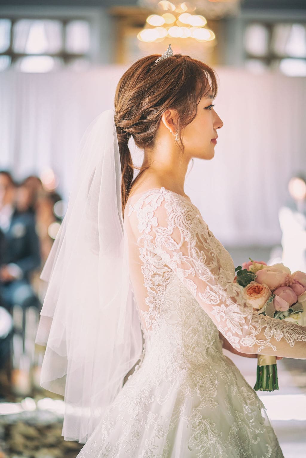 Bride holding hands with the groom during their wedding vows surrounded by family and friends.