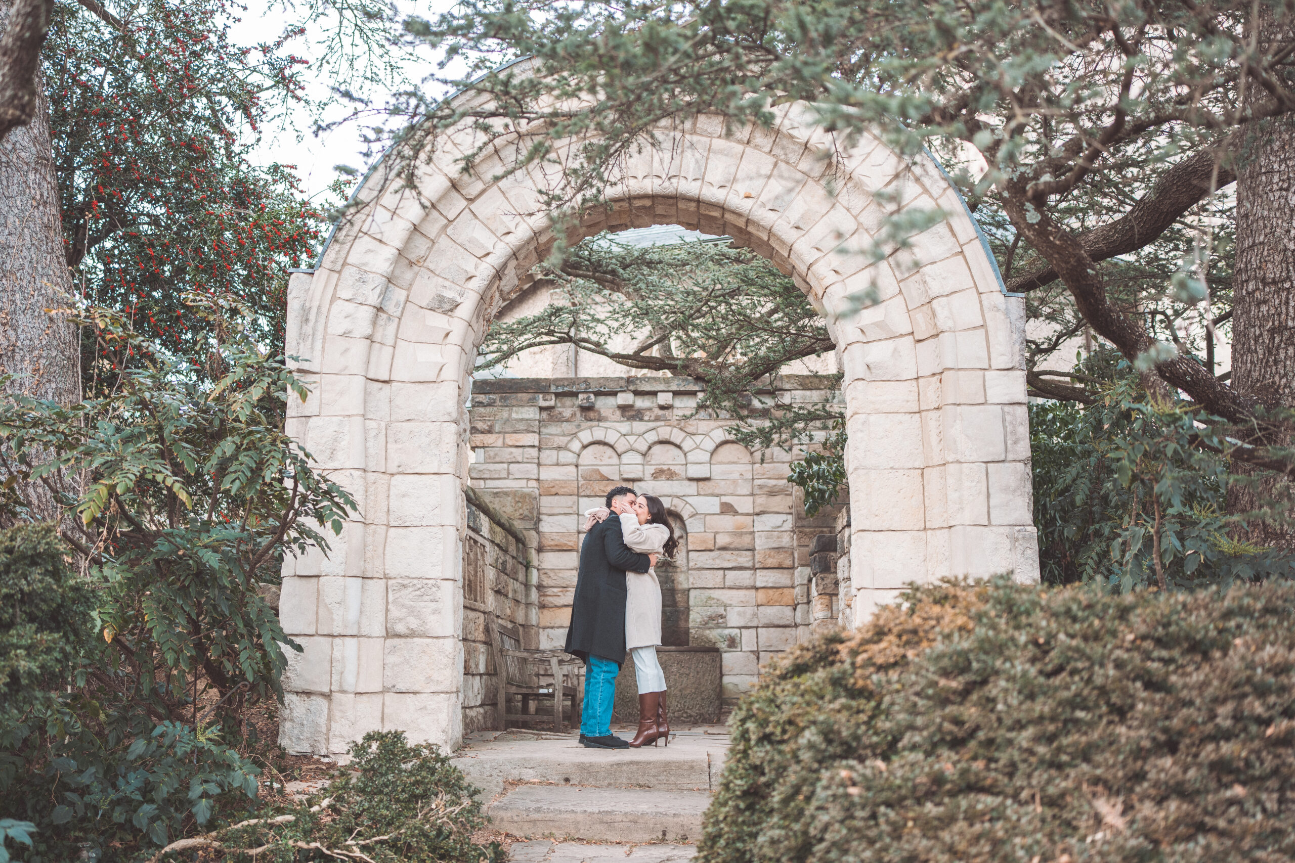 Couple embracing beneath a stone archway at Washington National Cathedral after their proposal.