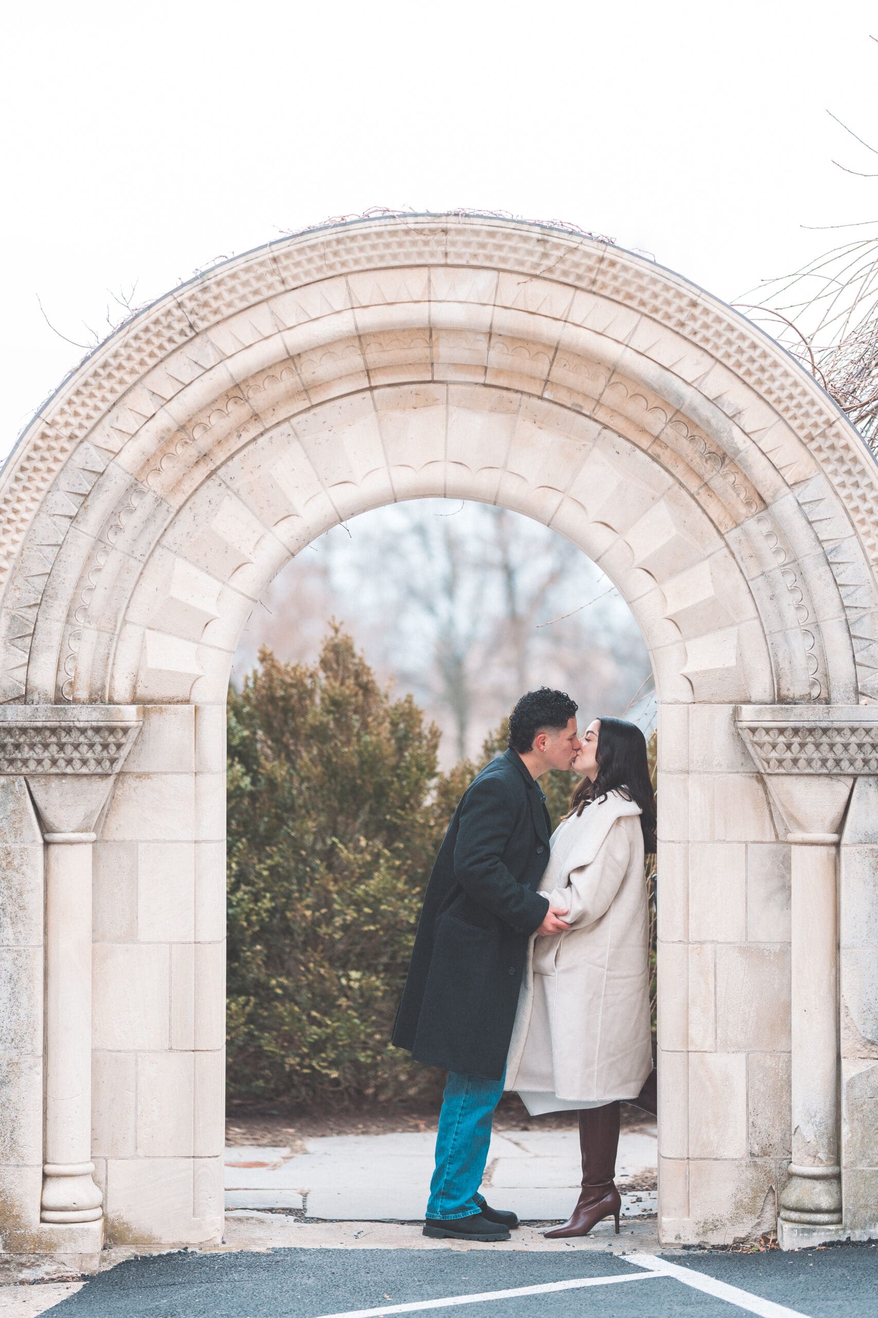 Couple kissing beneath a stone archway at Washington National Cathedral after their proposal.