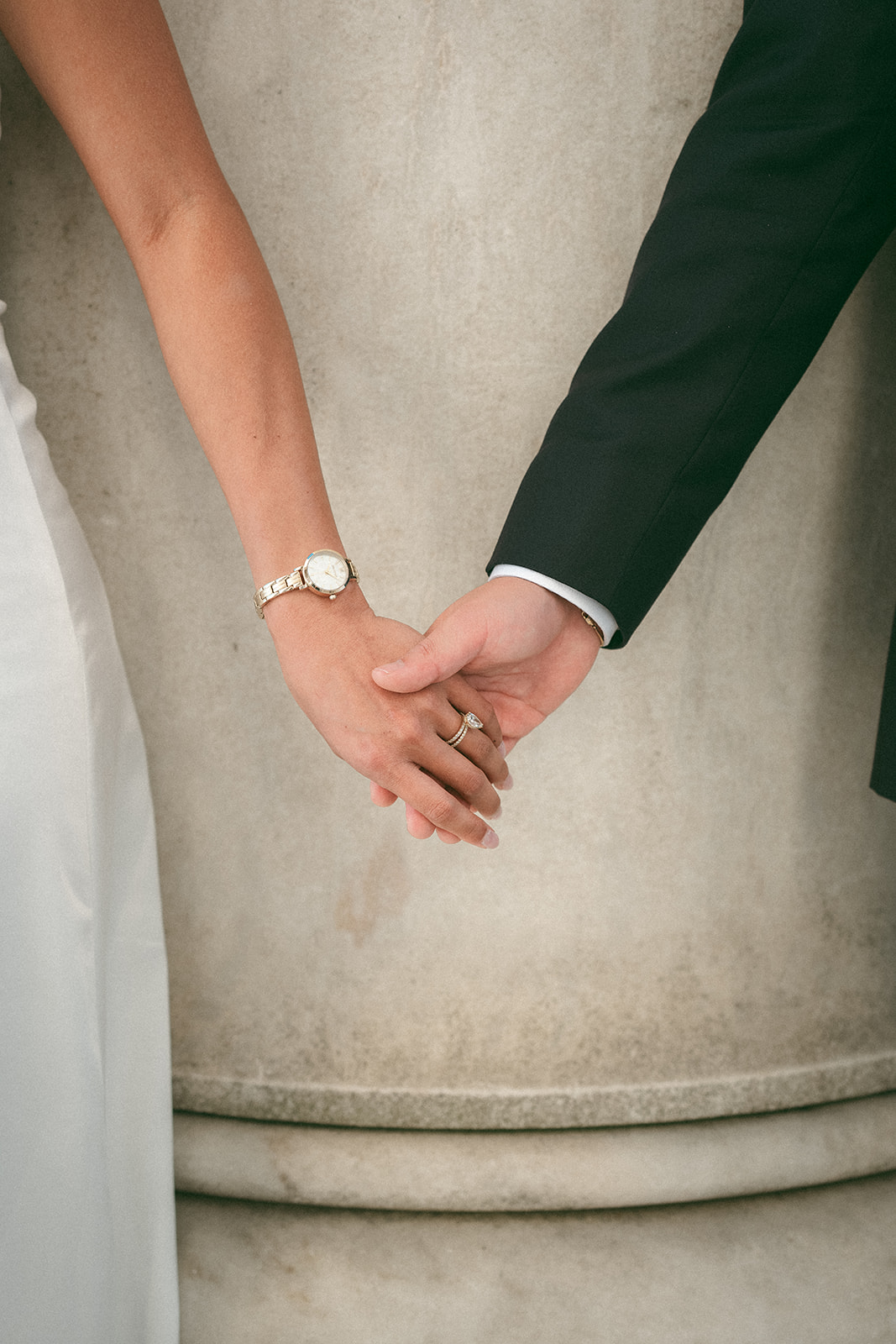 Close-up of the bride and groom holding hands showing her engagement ring.