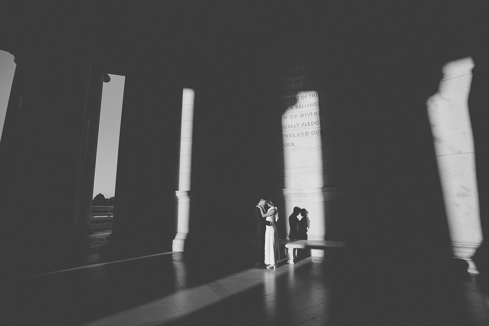 Black and white portrait of the couple embracing inside the Jefferson Memorial with dramatic light and shadows.