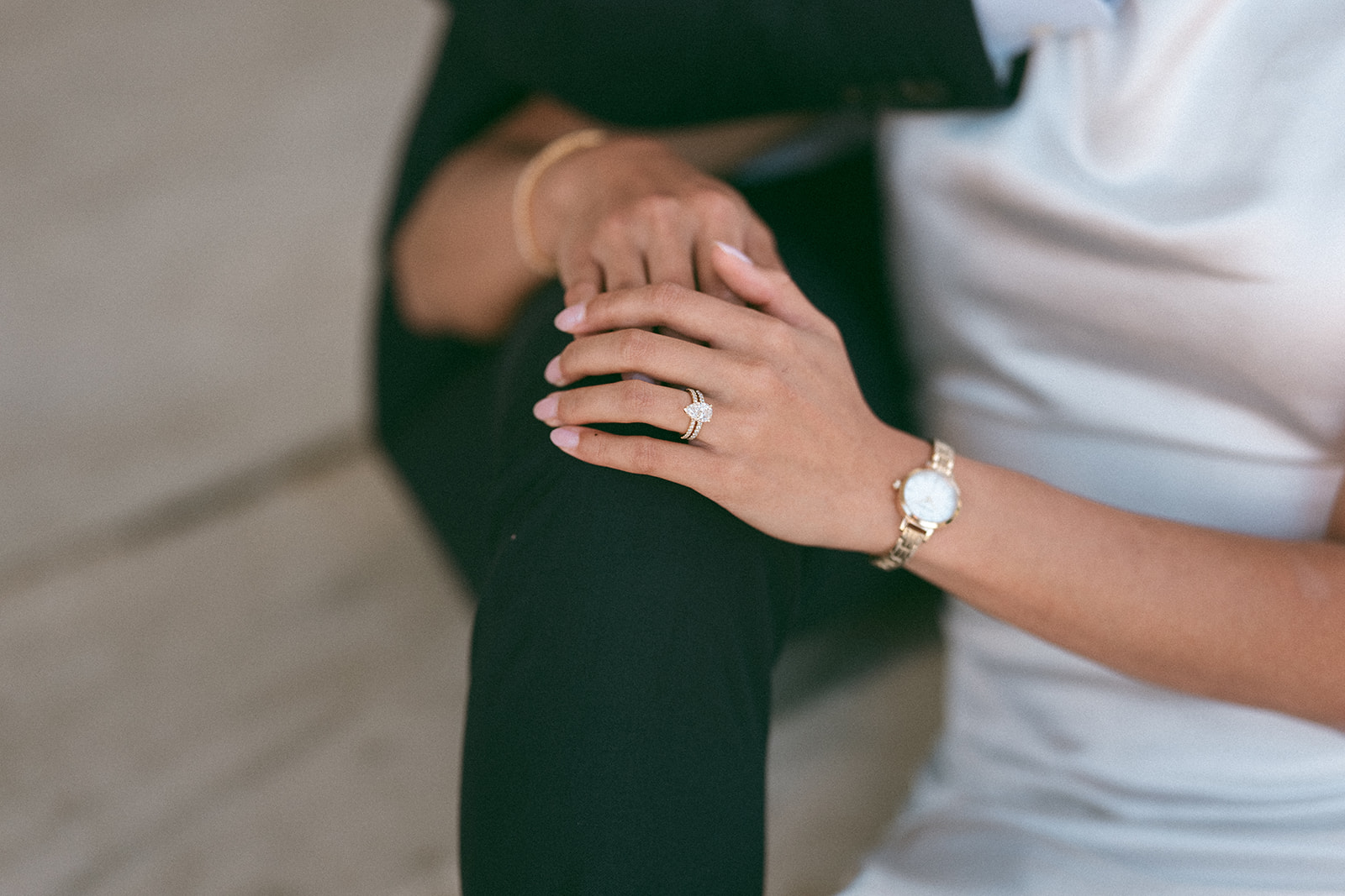 Close-up of the bride's hand showing her engagement ring while holding her partner's arm.