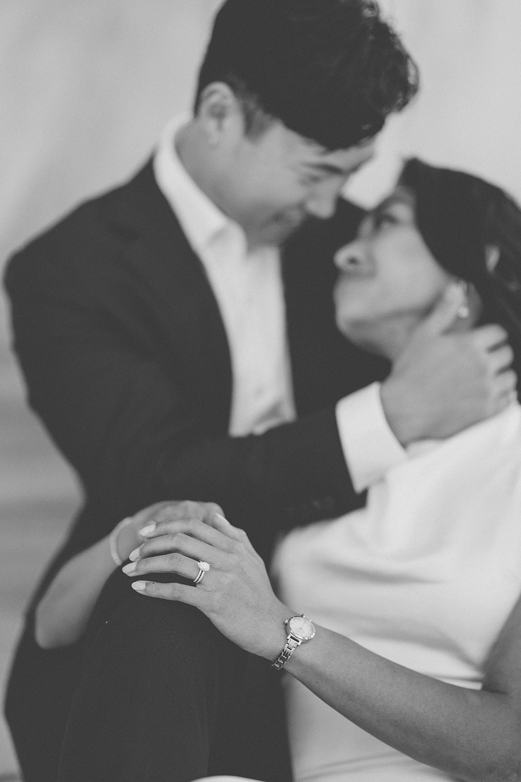 Black and white close-up of an engagement ring as the couple embraces.