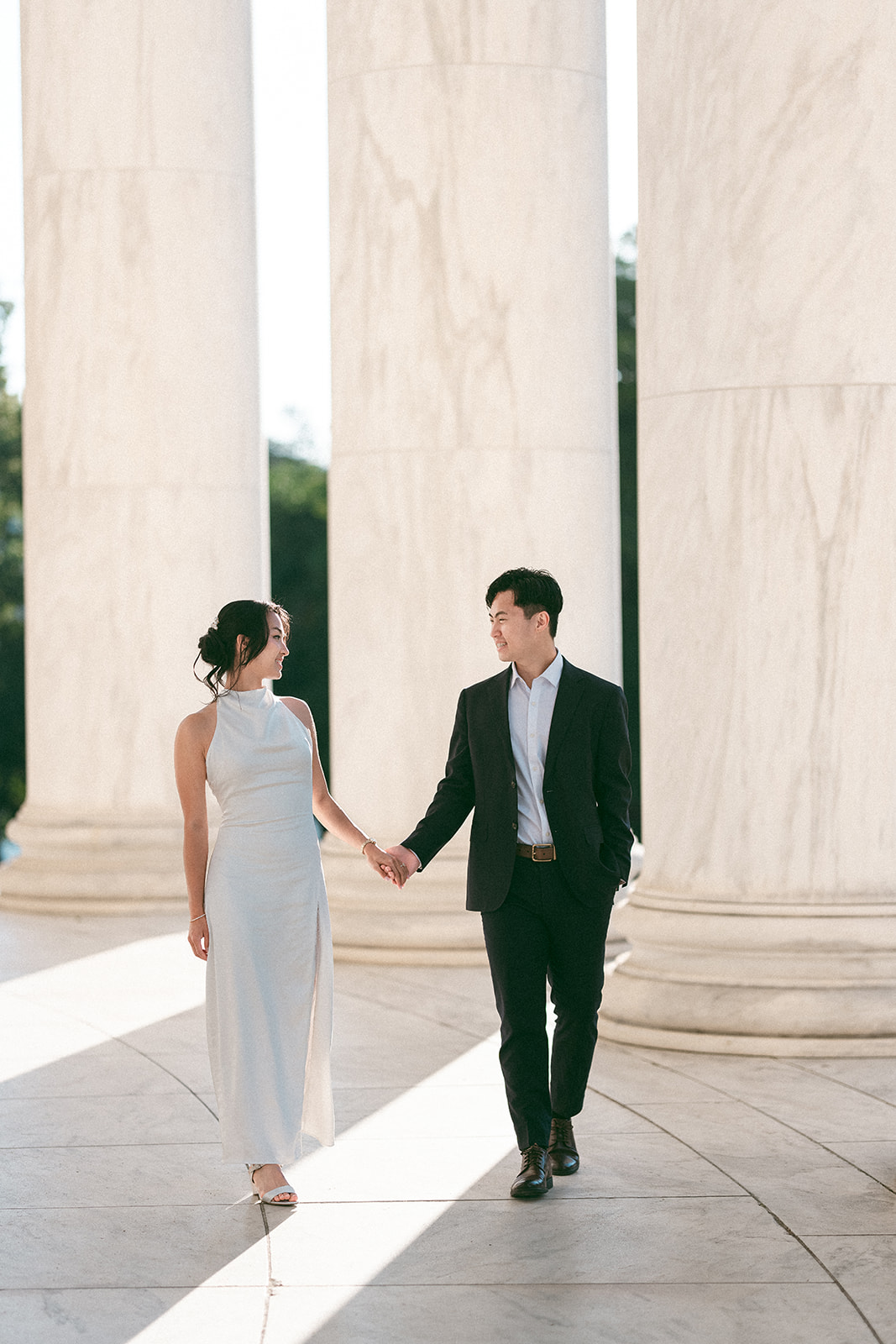 Couple holding hands while walking beneath the Jefferson Memorial columns.