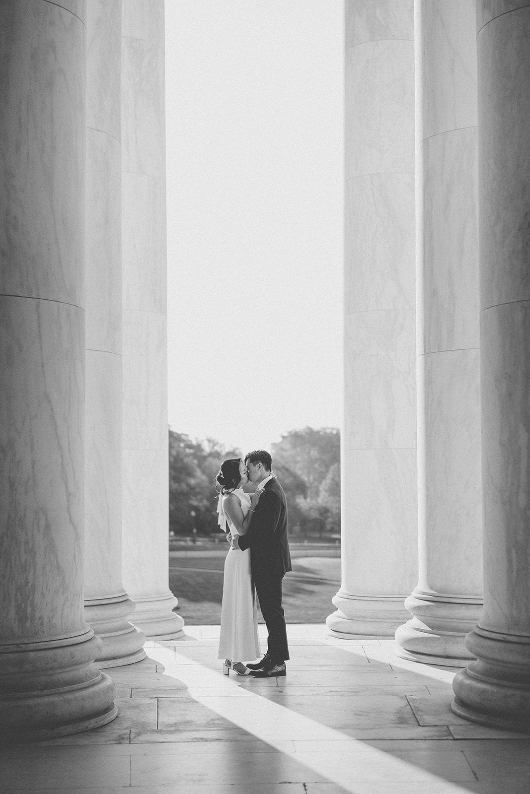 Black and white portrait of the couple kissing between the Jefferson Memorial columns during a Washington DC engagement session.