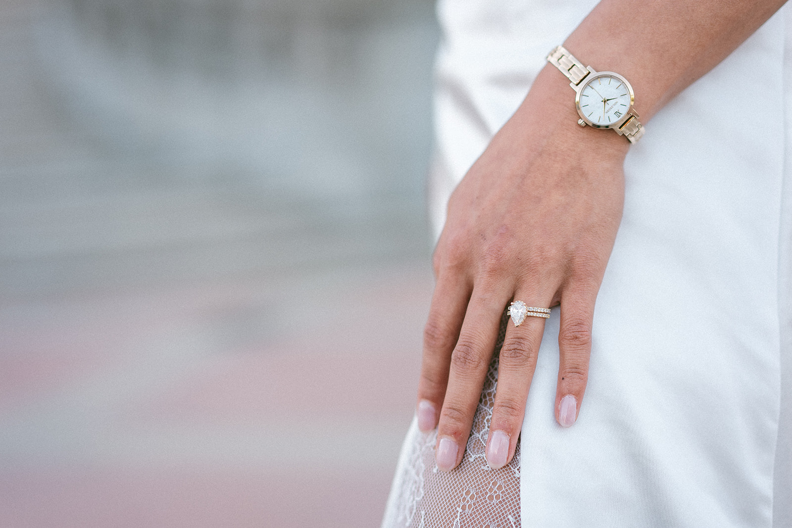 Close-up of the bride's engagement ring and wedding band resting on her dress.