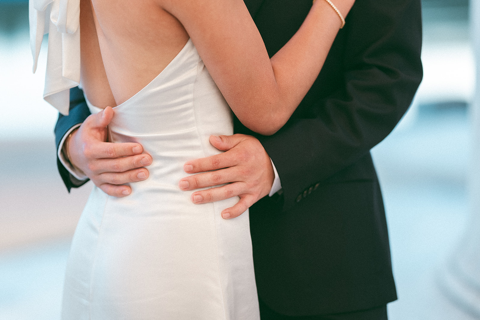 Close-up of the groom embracing the bride from behind.