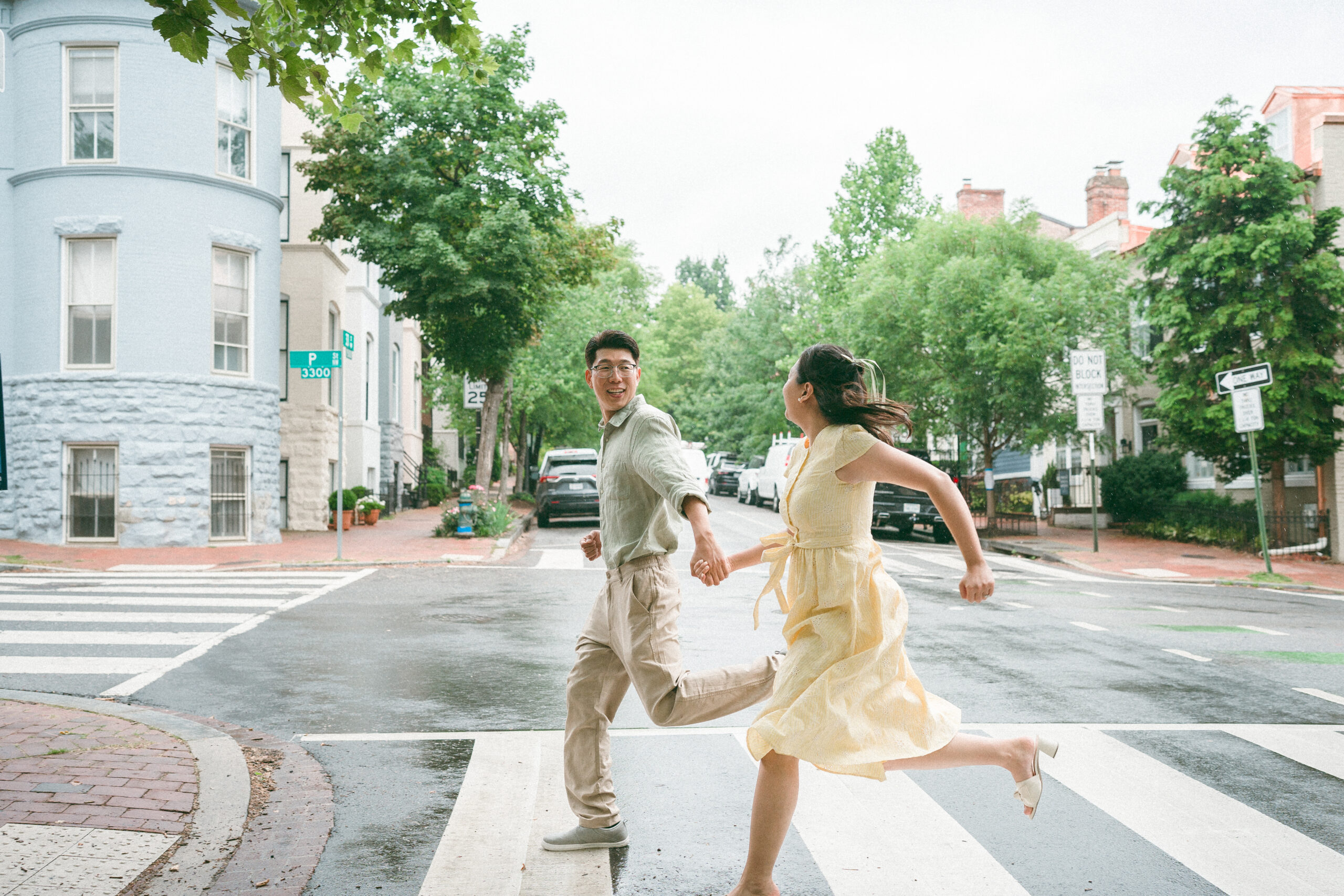 Couple running hand in hand across a crosswalk on a quiet rainy street.