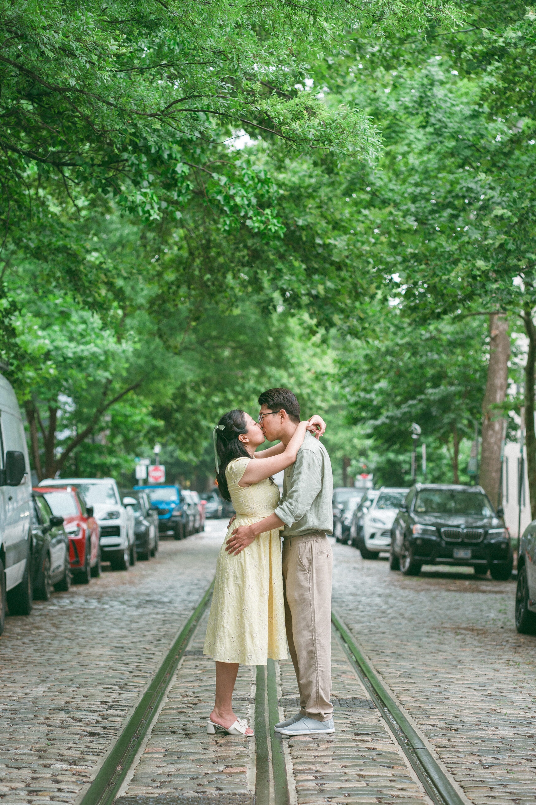 Couple sharing a kiss in the middle of a cobblestone street during rainy engagement photos.