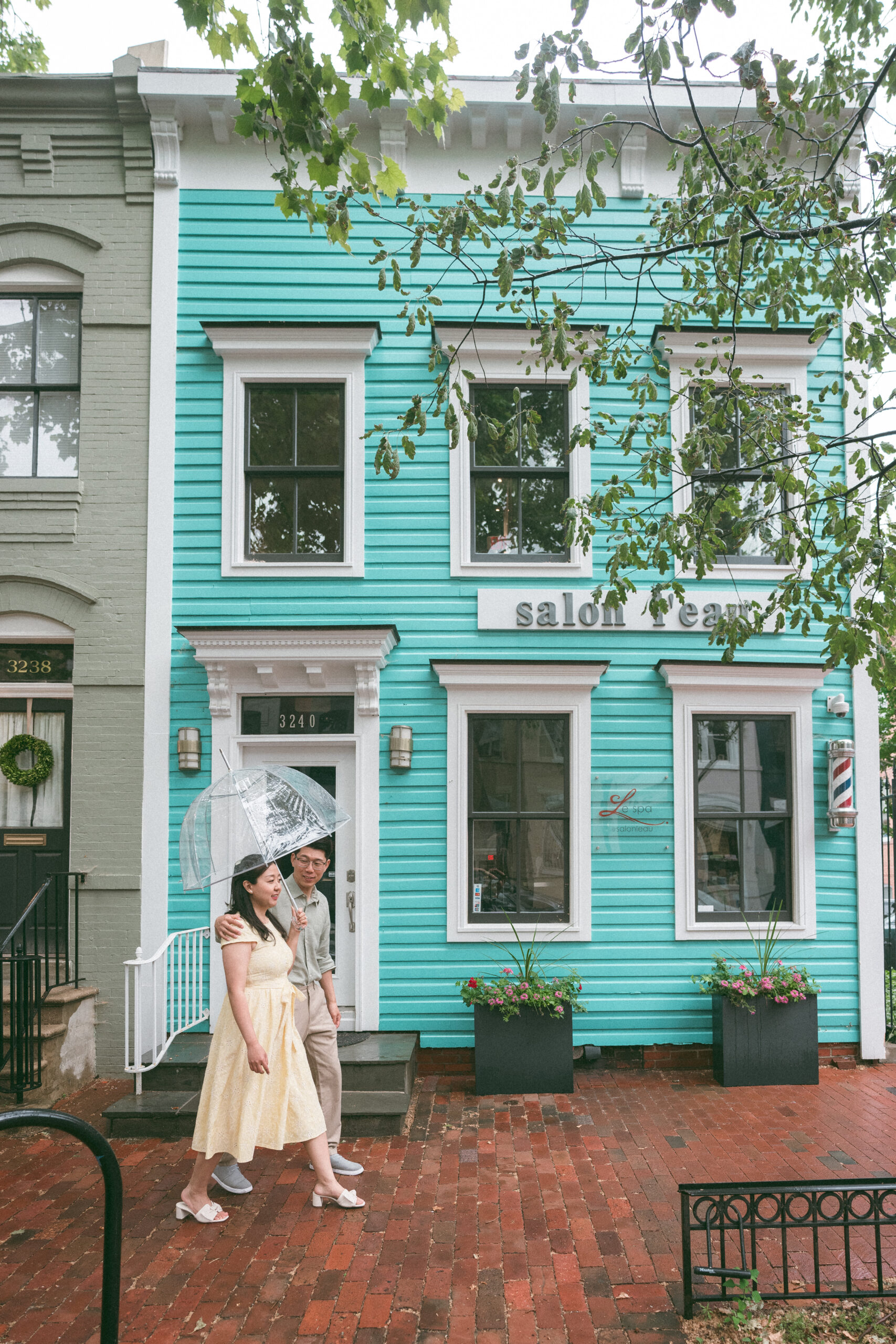 Couple walking beneath a clear umbrella in front of a colorful historic storefront.