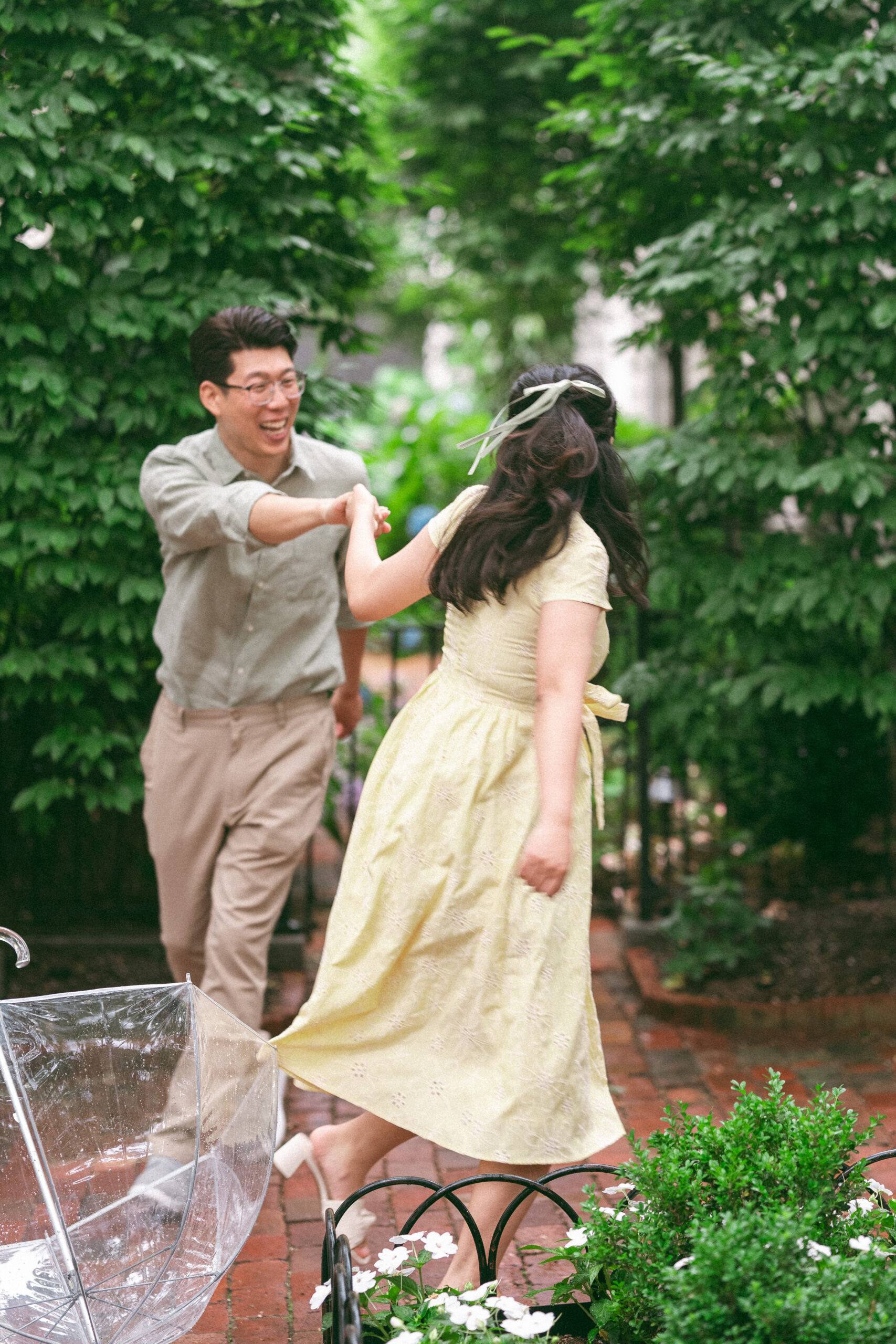 Couple running toward each other and laughing in a lush garden courtyard during rainy engagement photos.