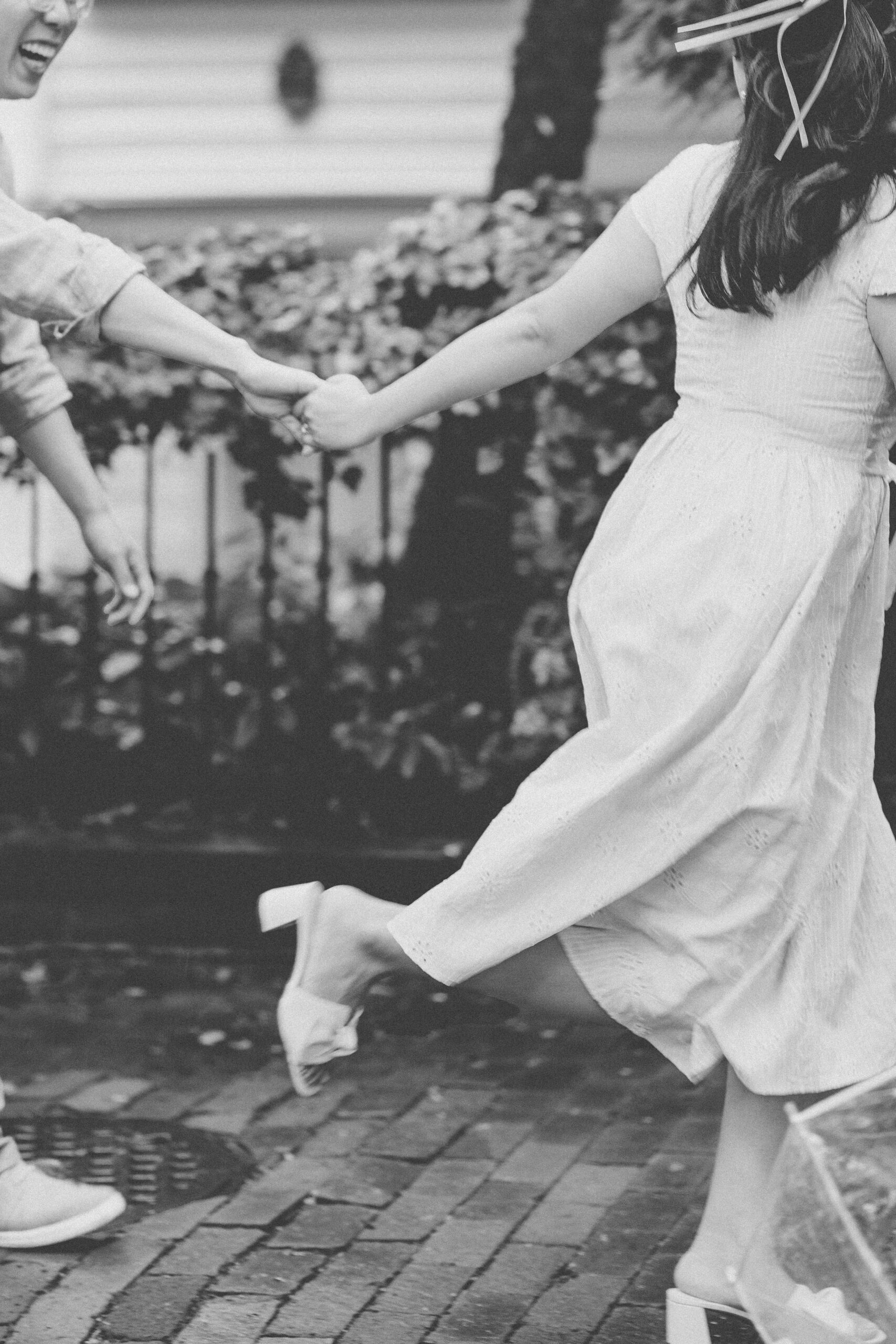 Black and white photo of the couple holding hands while running together on a rainy day.