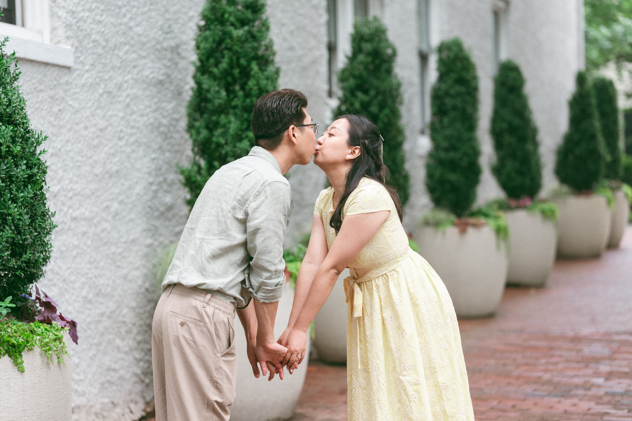 Couple leaning in for a playful kiss while holding hands outside a stone building.
