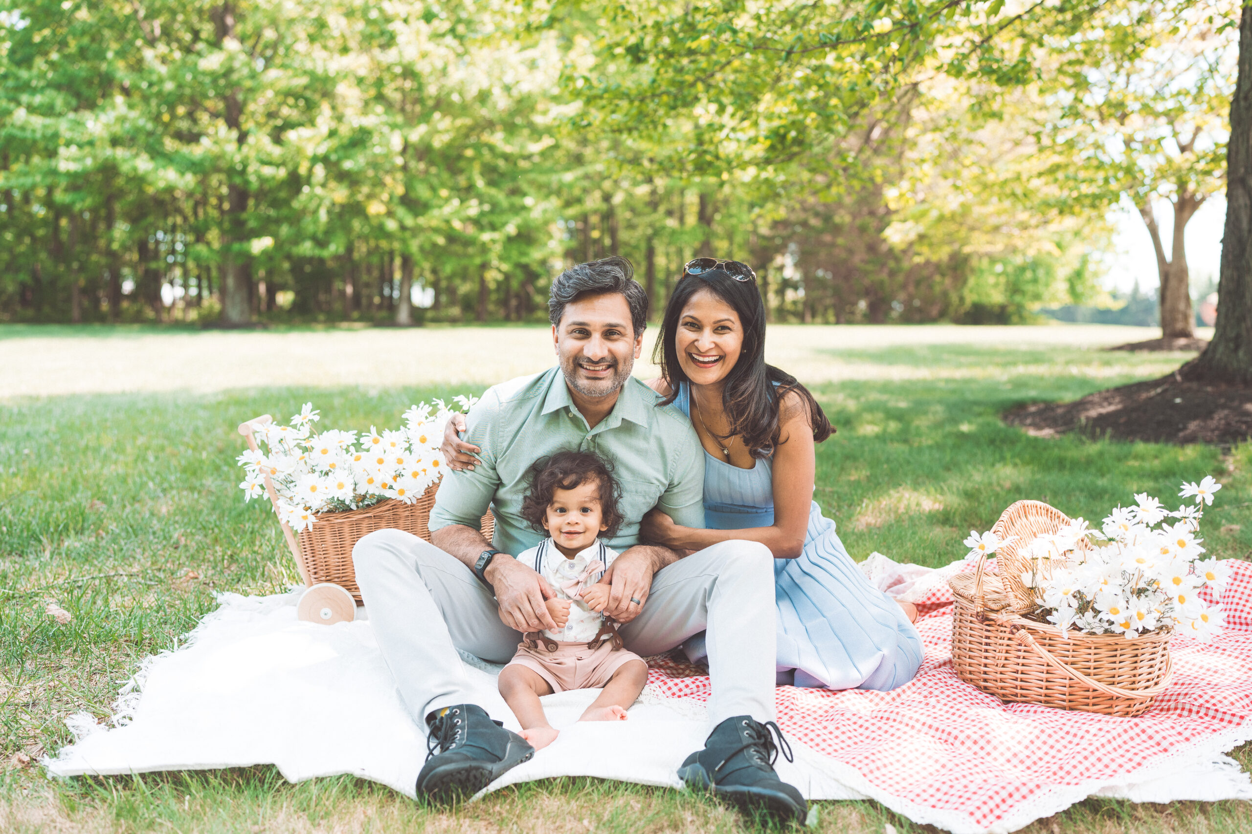 Family of three smiling together on a picnic blanket surrounded by flowers during a Maryland family photoshoot.