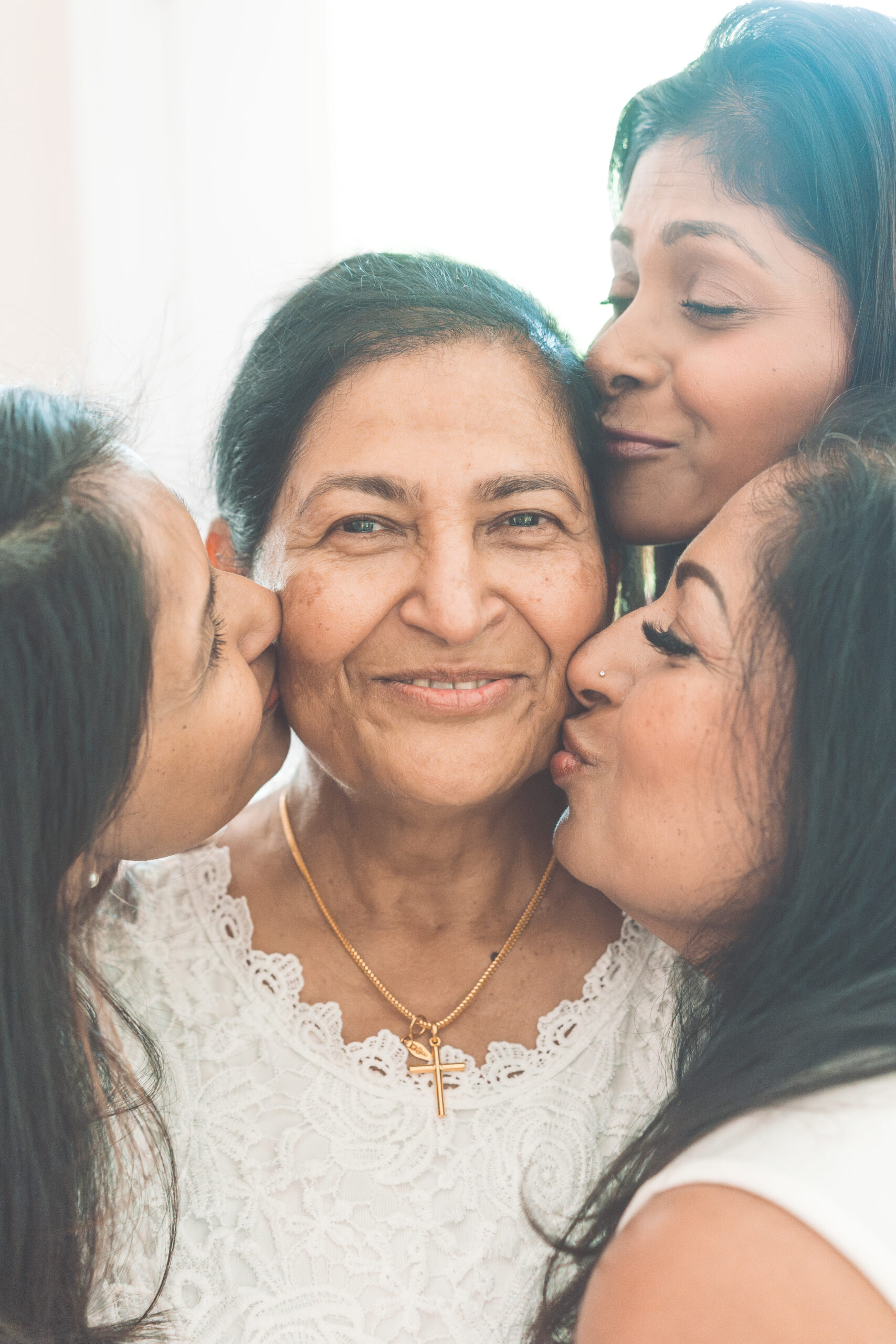 Three generations sharing a sweet portrait as daughters kiss their mother on the cheeks.