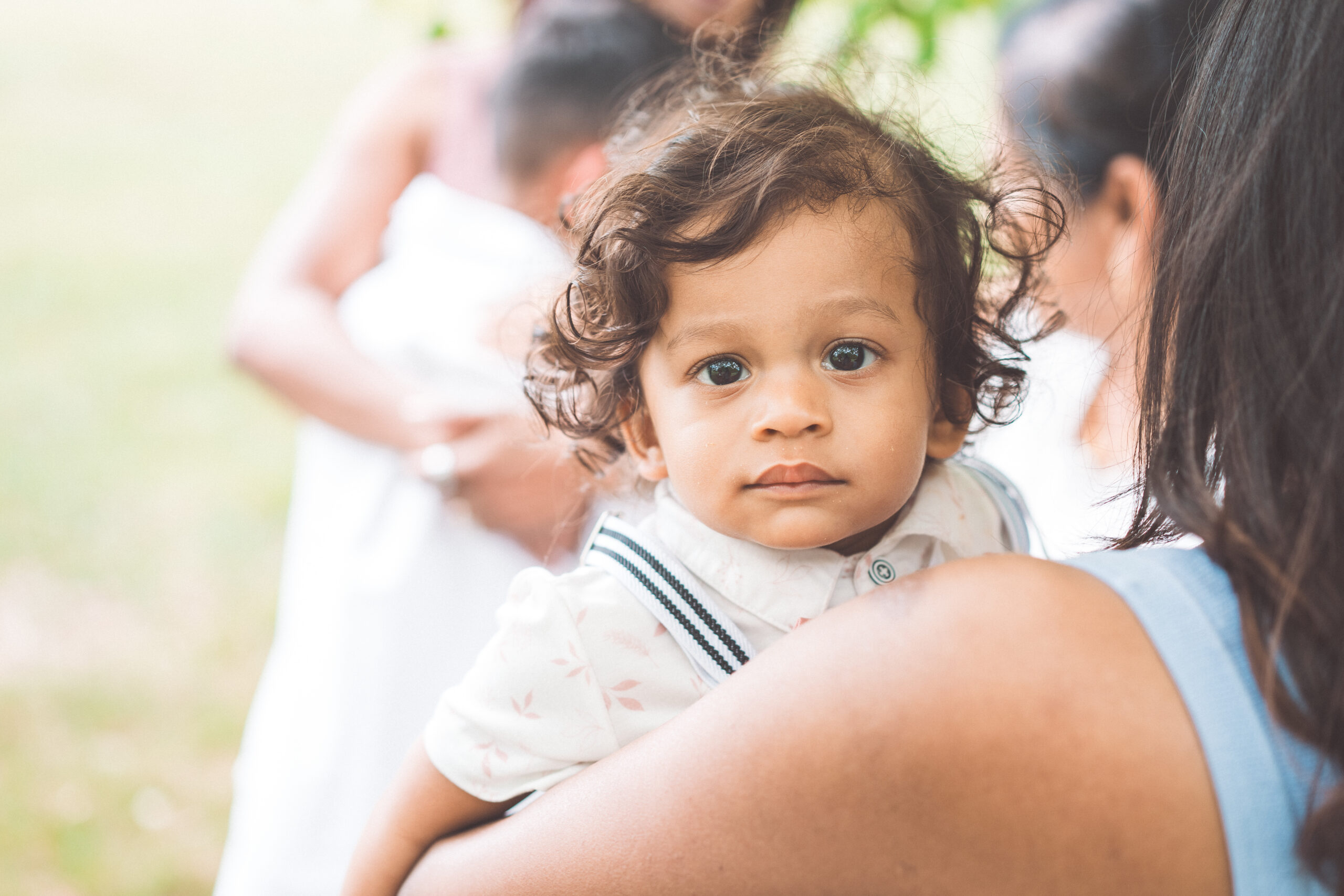 Toddler looking at the camera while being held by a parent during an outdoor family gathering.