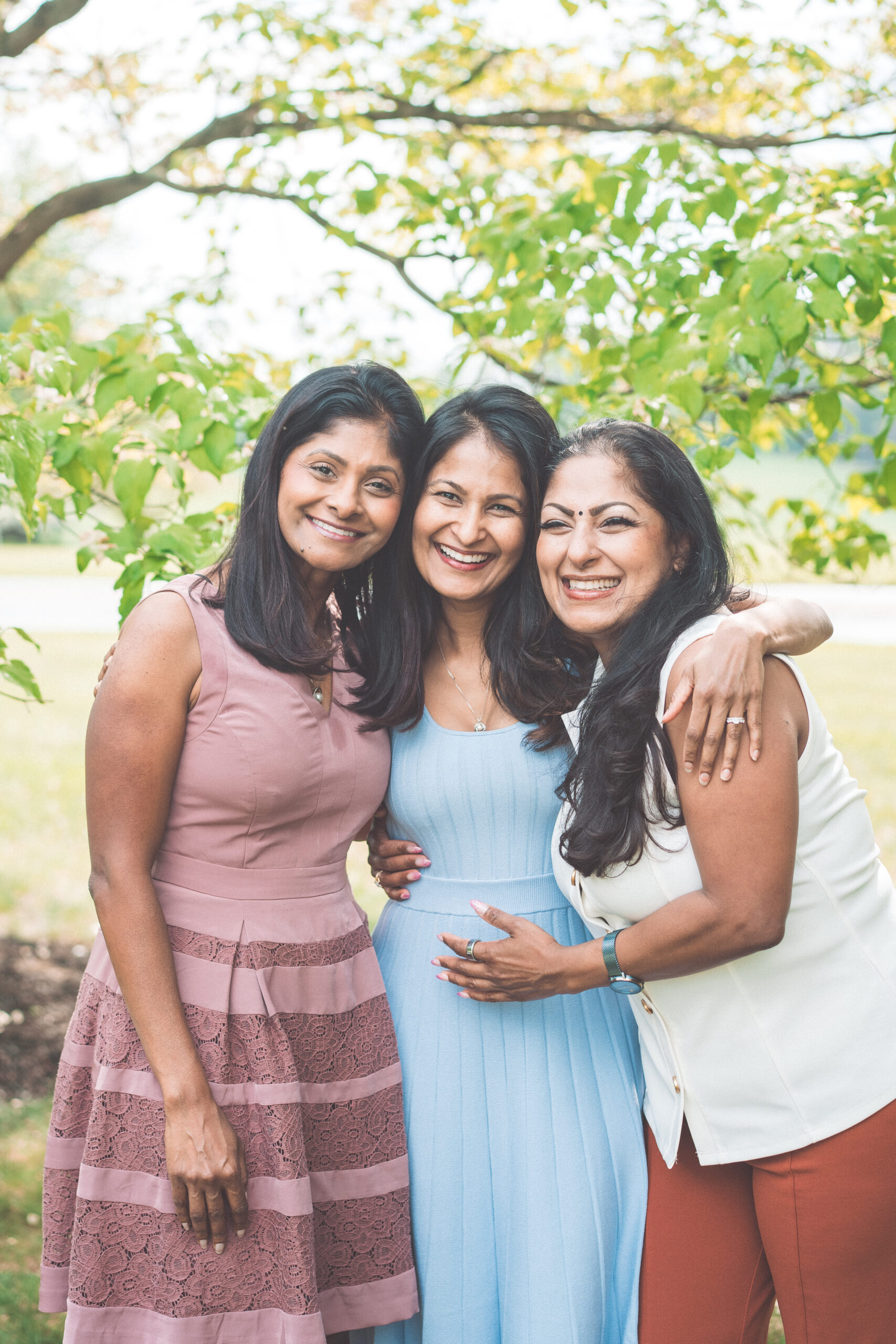 Three sisters embracing and smiling together during a Maryland family photoshoot in the park.