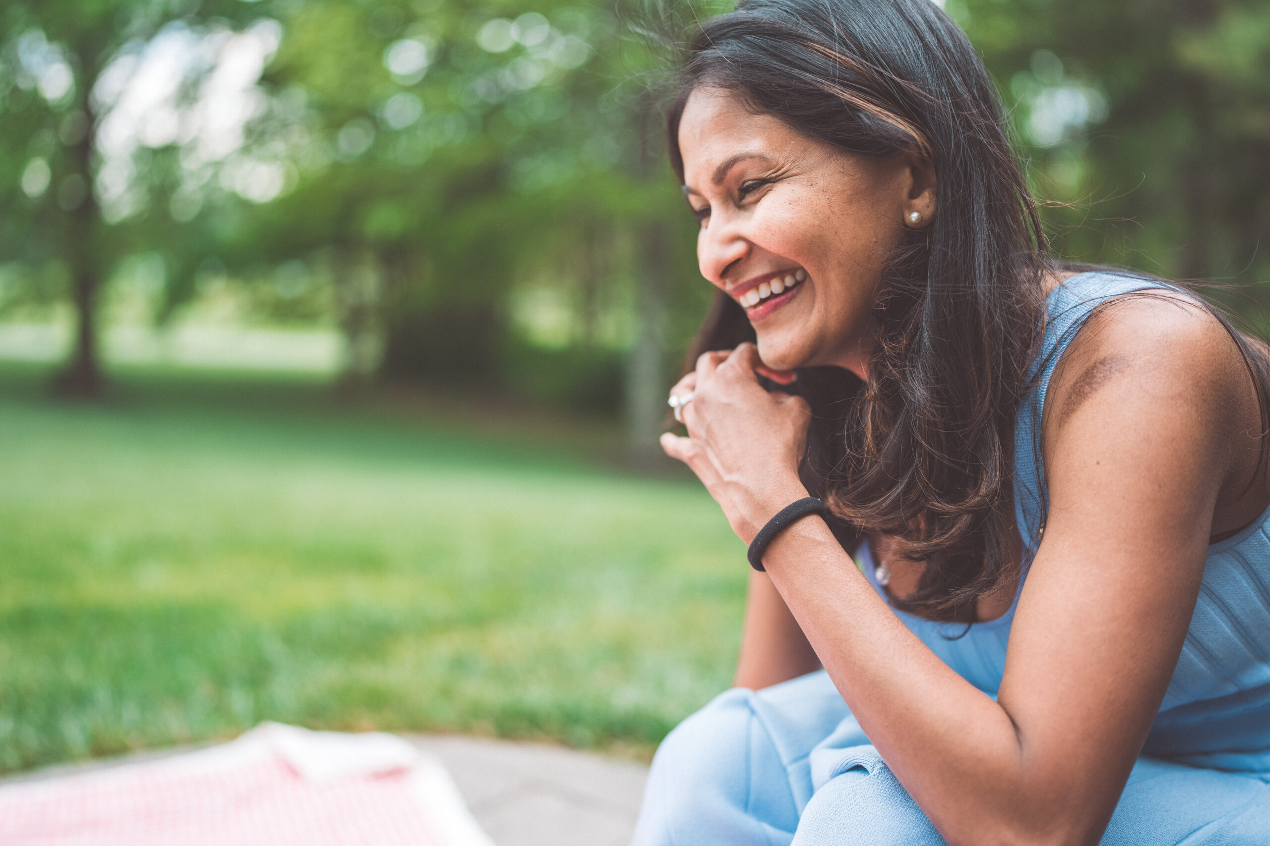 Mom laughing during a candid family picnic surrounded by green trees.