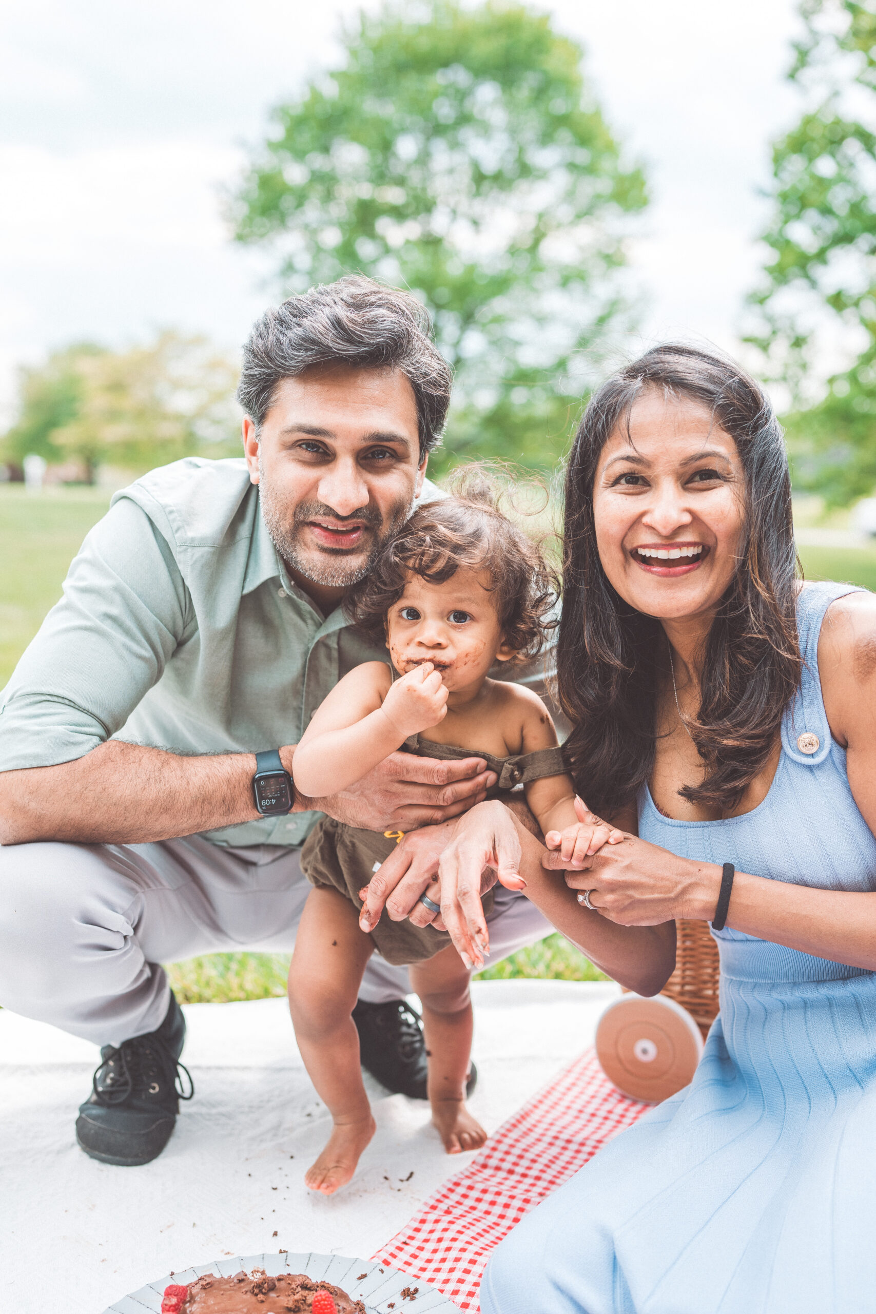 Parents posing with their cake smash toddler after a messy first birthday celebration during a Maryland family photoshoot.